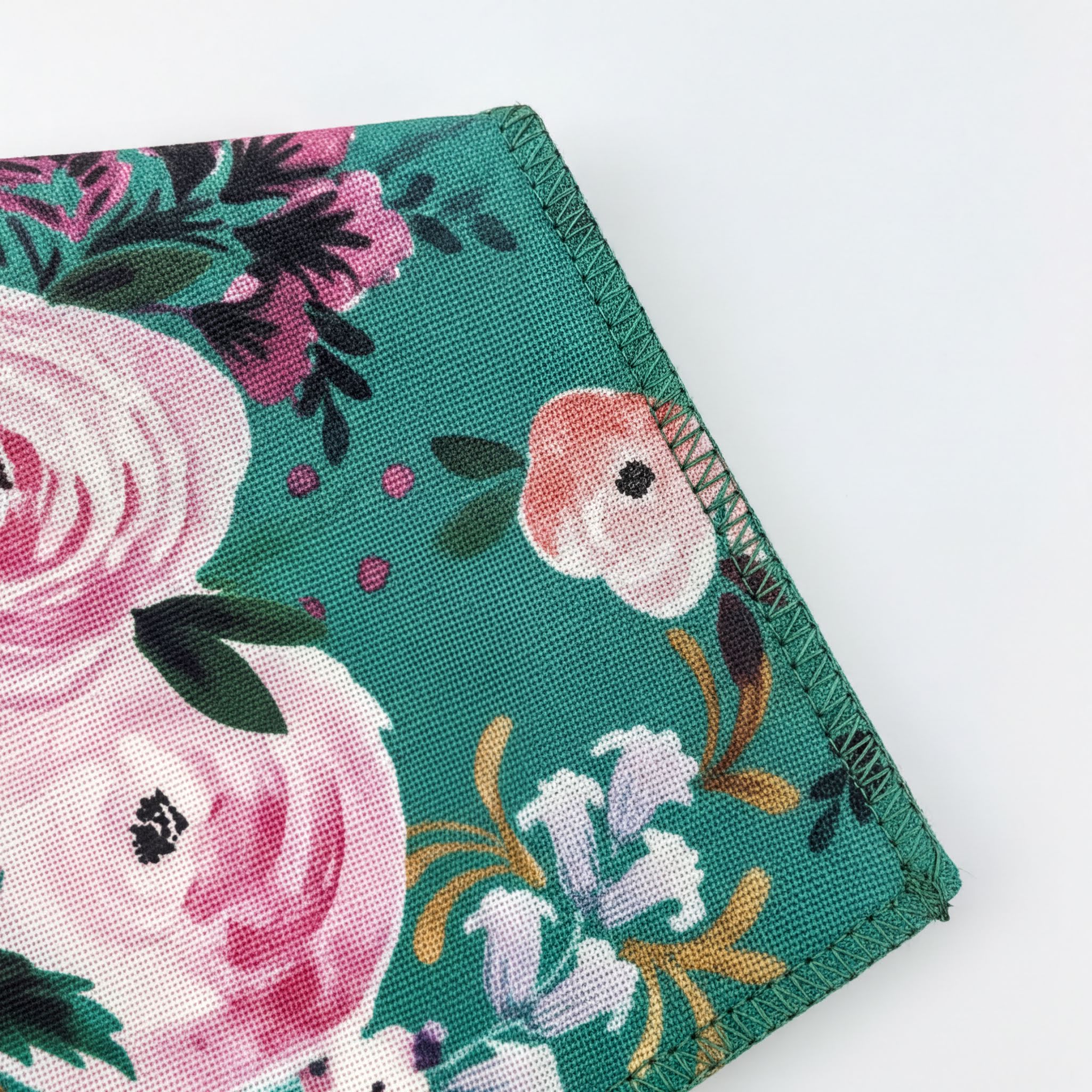 a close-up view of a pocket square with a floral pattern, featuring pink and white flowers, green leaves, and a dark green background.