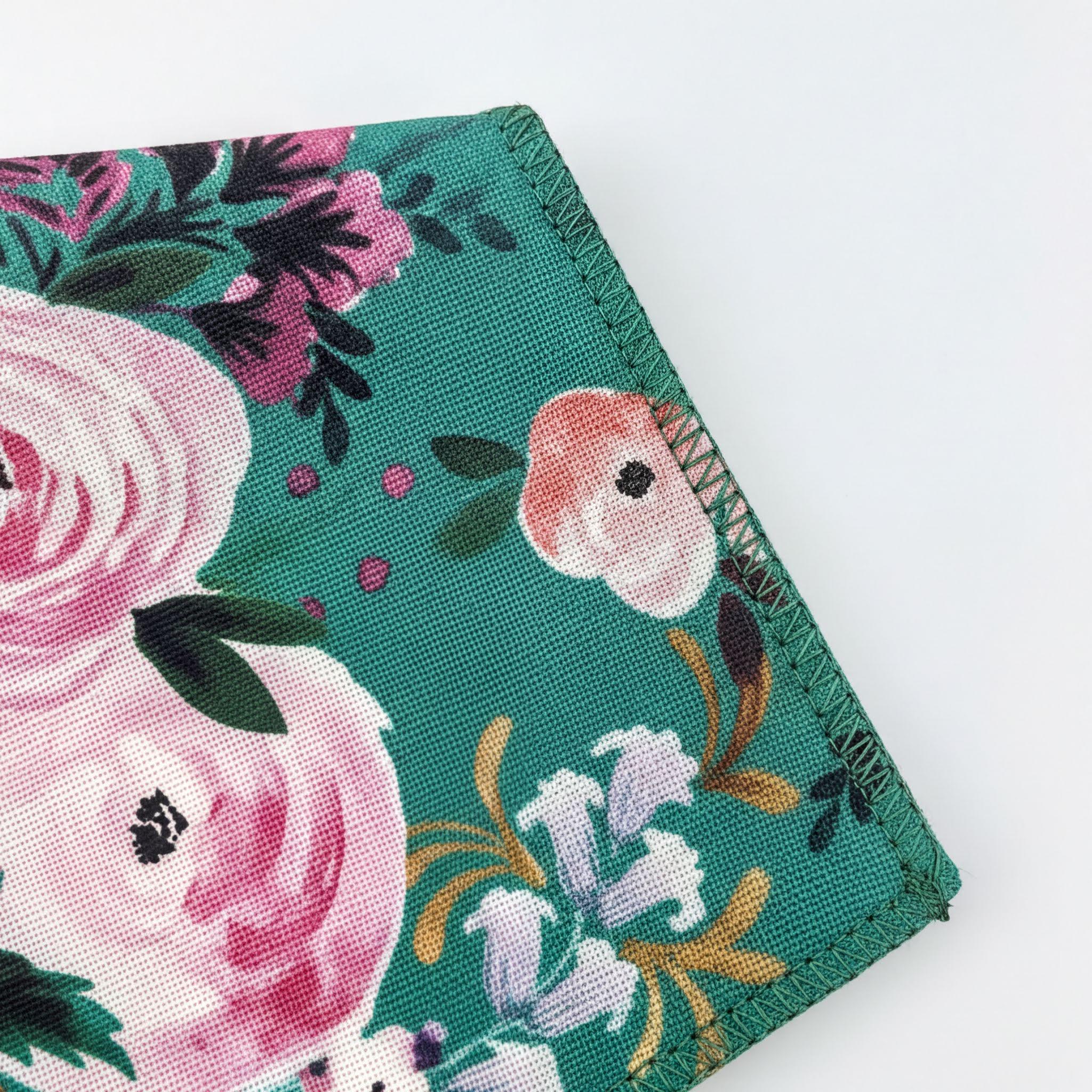 a close-up view of a pocket square with a floral pattern, featuring pink and white flowers, green leaves, and a dark green background.