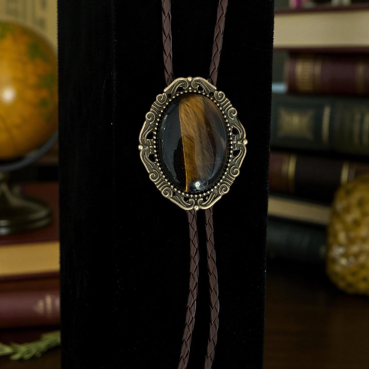 a close-up of a decorative pendant with a feather design, hanging on a black stand.