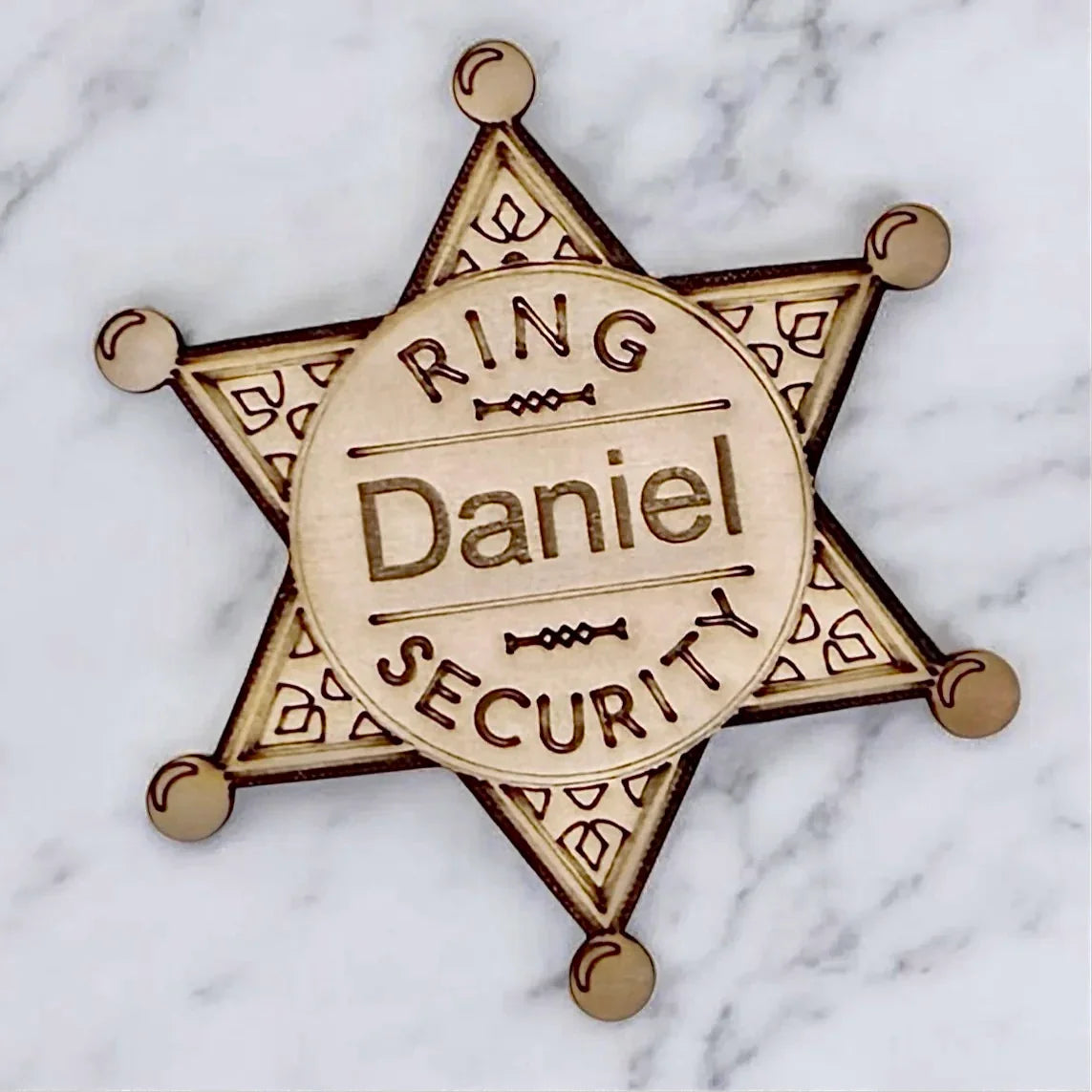 Wooden Ring Security Badge, with the name "Daniel" star-shaped, which is offered as an add-on to orders, if desired, for ring bearer badges. It says "ring security." Size 3 1/4 inches tall, easy pin style, perfect ring bearer gift idea.