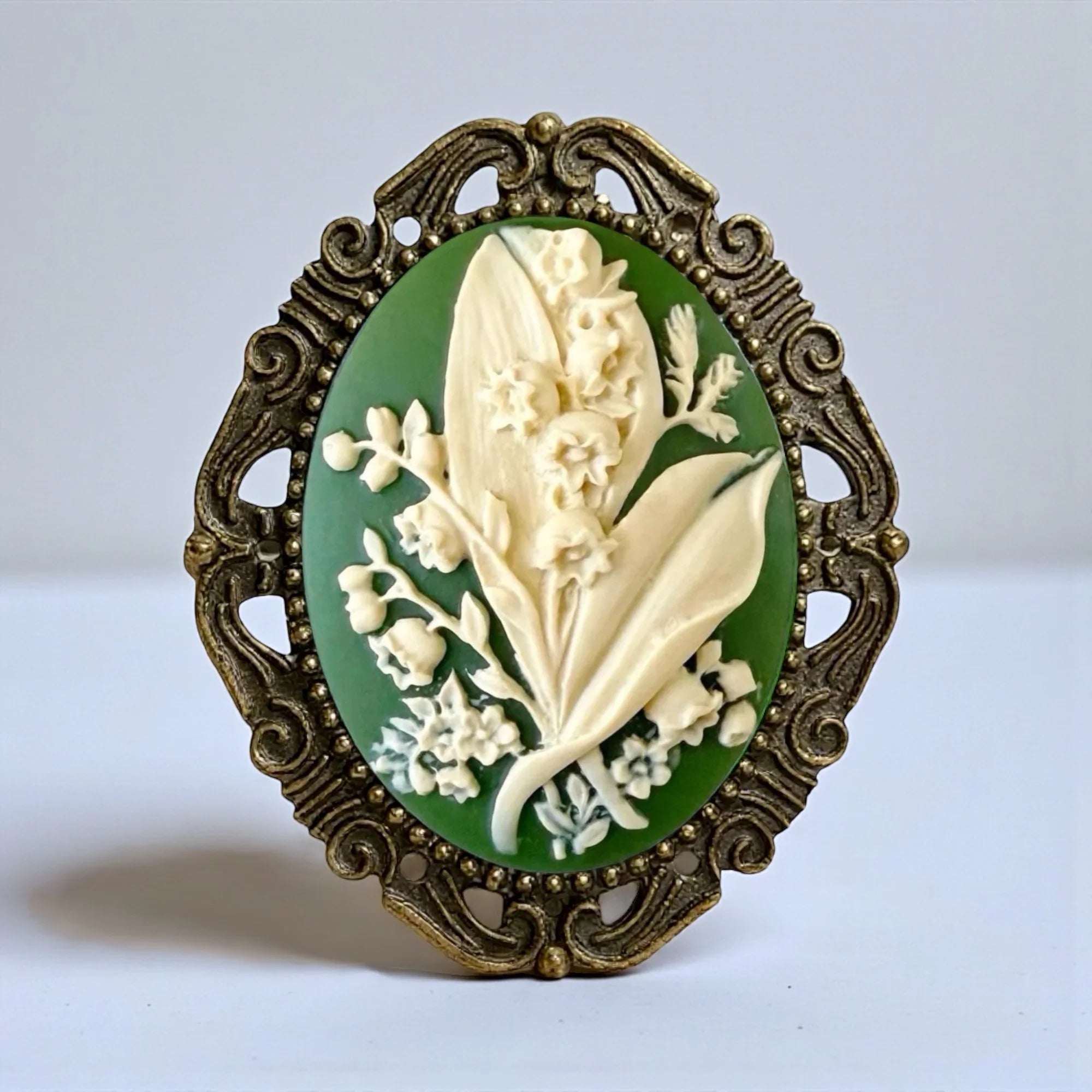 Floral brooch with green and ivory floral design and bronze frame on a light background