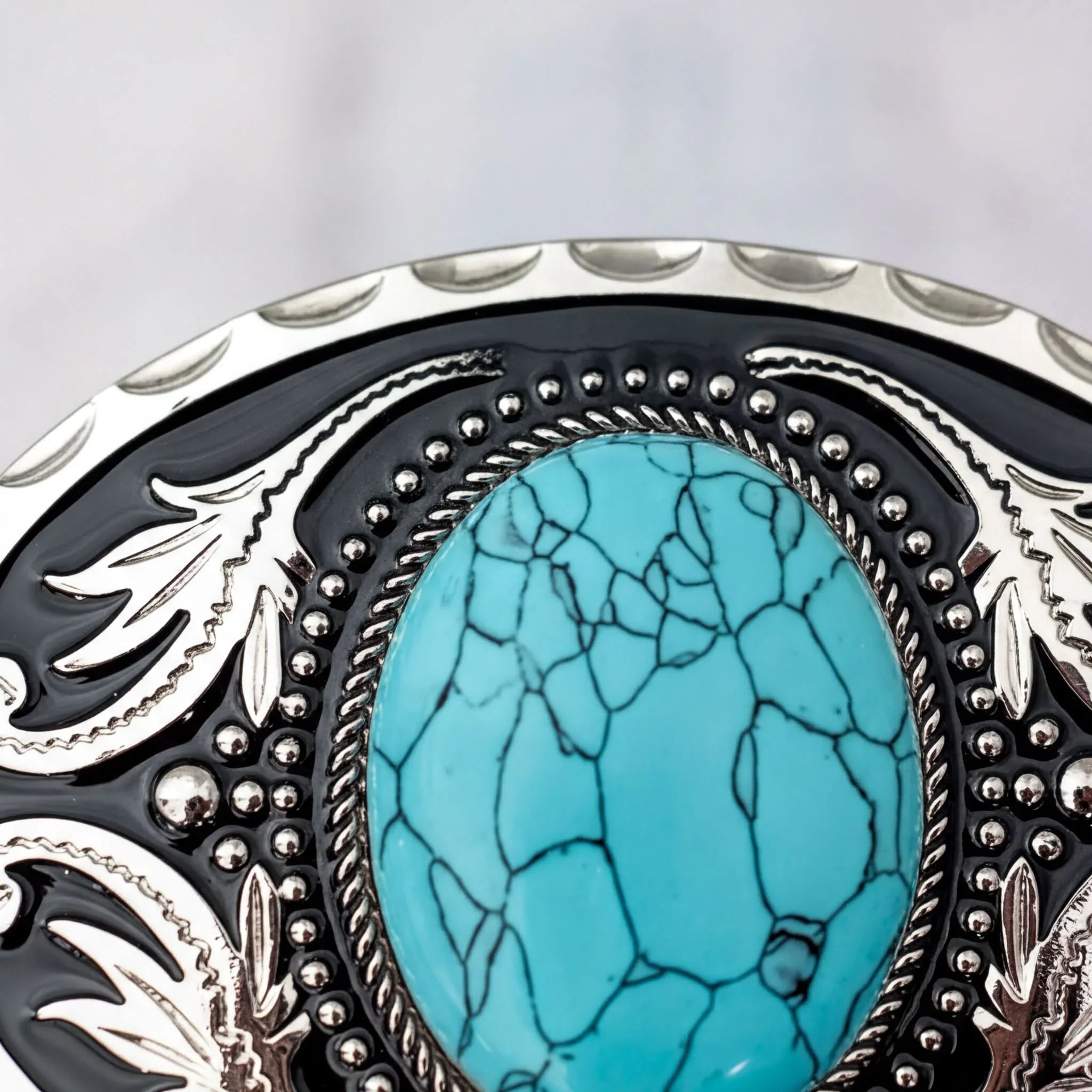 A close-up image of a decorative black and silver belt buckle with a large turquoise stone in the center.