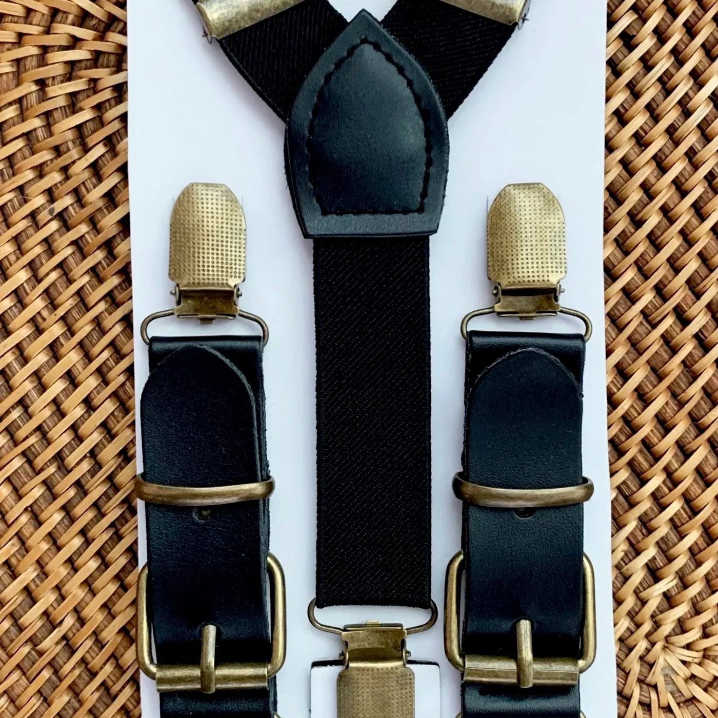 Black suspenders for groomsmen with bronze clips on a white card against a woven background