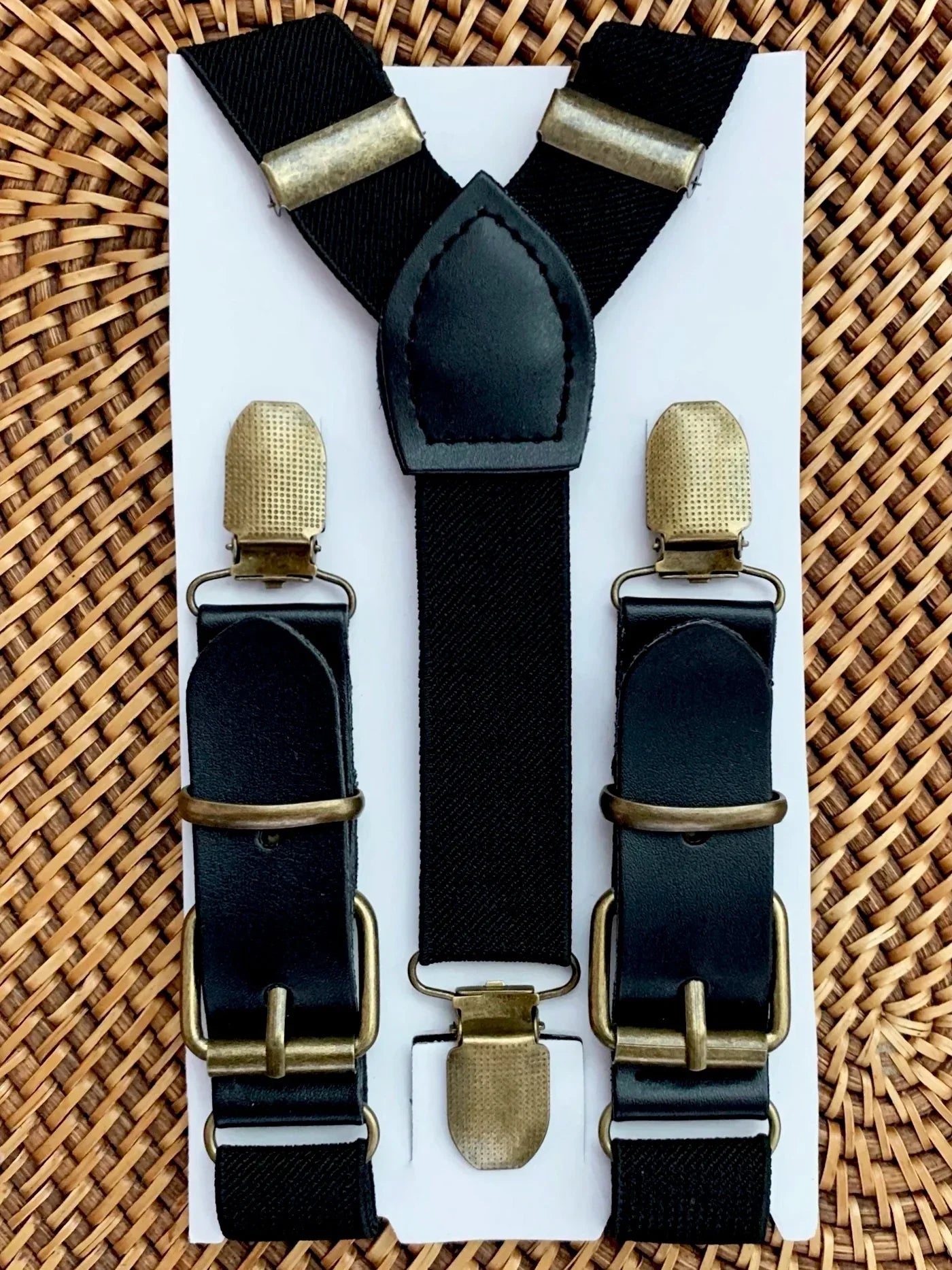 Black suspenders for groomsmen with bronze clips on a white card against a woven background