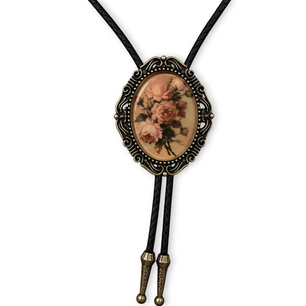 A vintage bolo tie necklace featuring a black leather braided cord, an ornate antique bronze oval frame, and a central floral medallion with pink roses on a beige background.