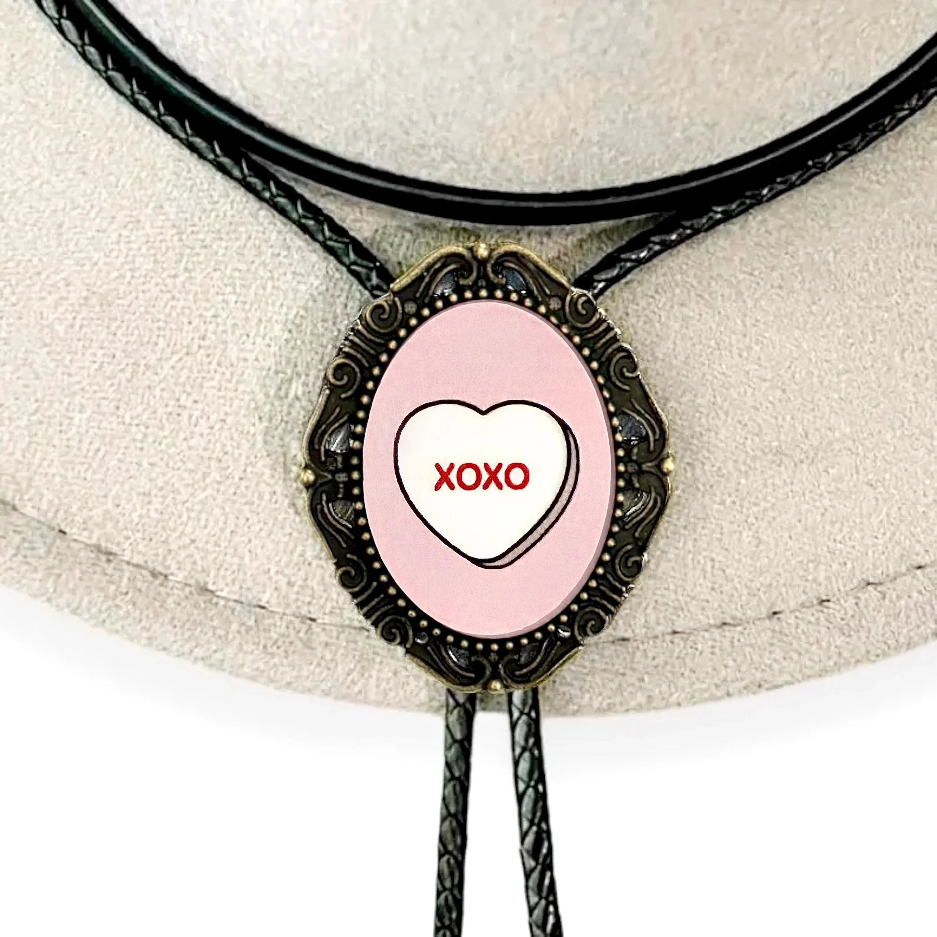 Infographic from The Bold Bow Tie titled Bolo Tie Features. Right: A vintage-style bolo tie with a blue and white cowboy riding a horse illustration inside an ornate bronze filigree frame on a black braided cord. Left: Lines connect the image to three checkmark features: Handmade, 39" Long Cord, and Pendant is 1.5" (L) x 1.25" (W). Bottom text reads Perfect Addition to Your Outfit.