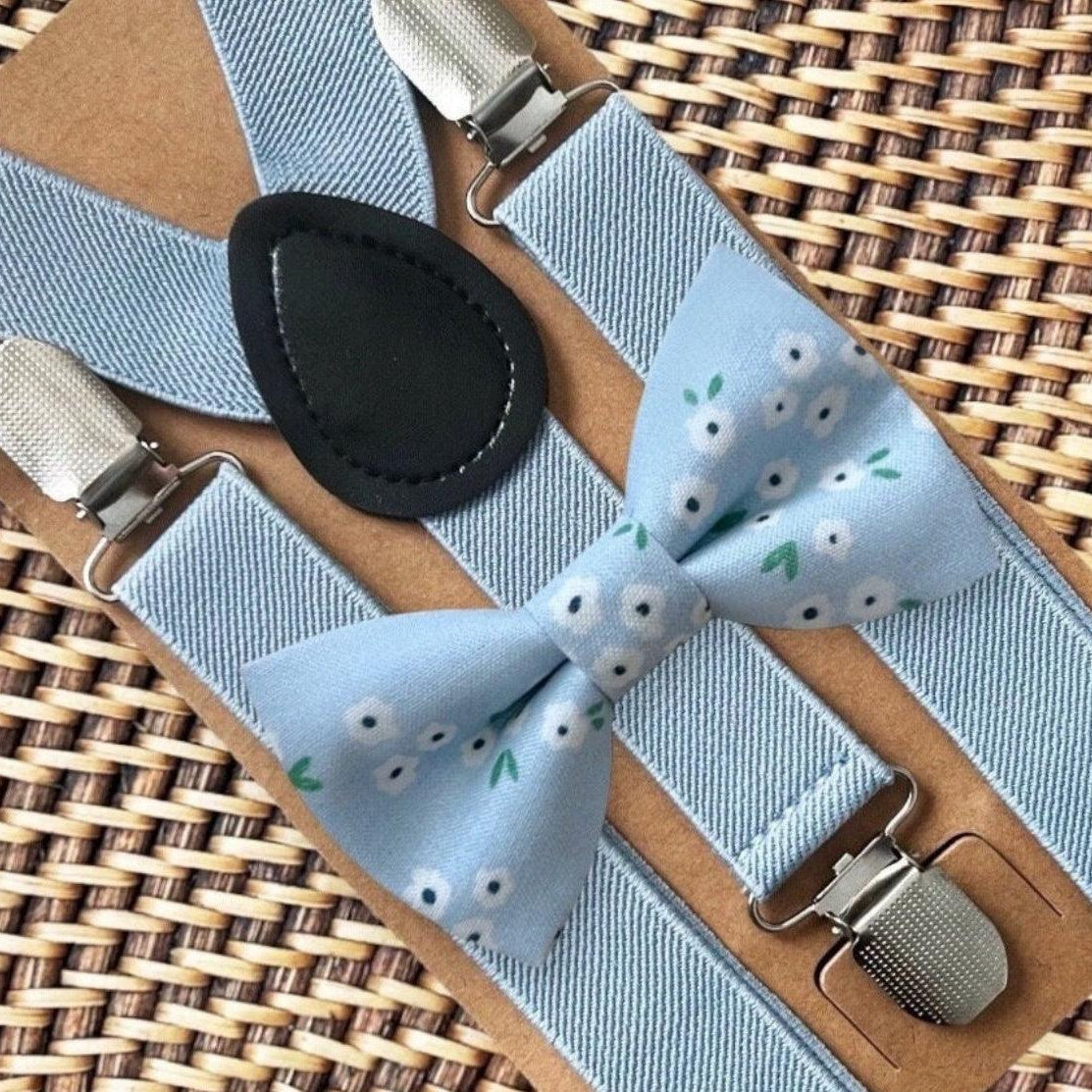 Dainty light blue daisy patterned bow tie with dusty blue suspenders and metal clips on a tan leather backdrop