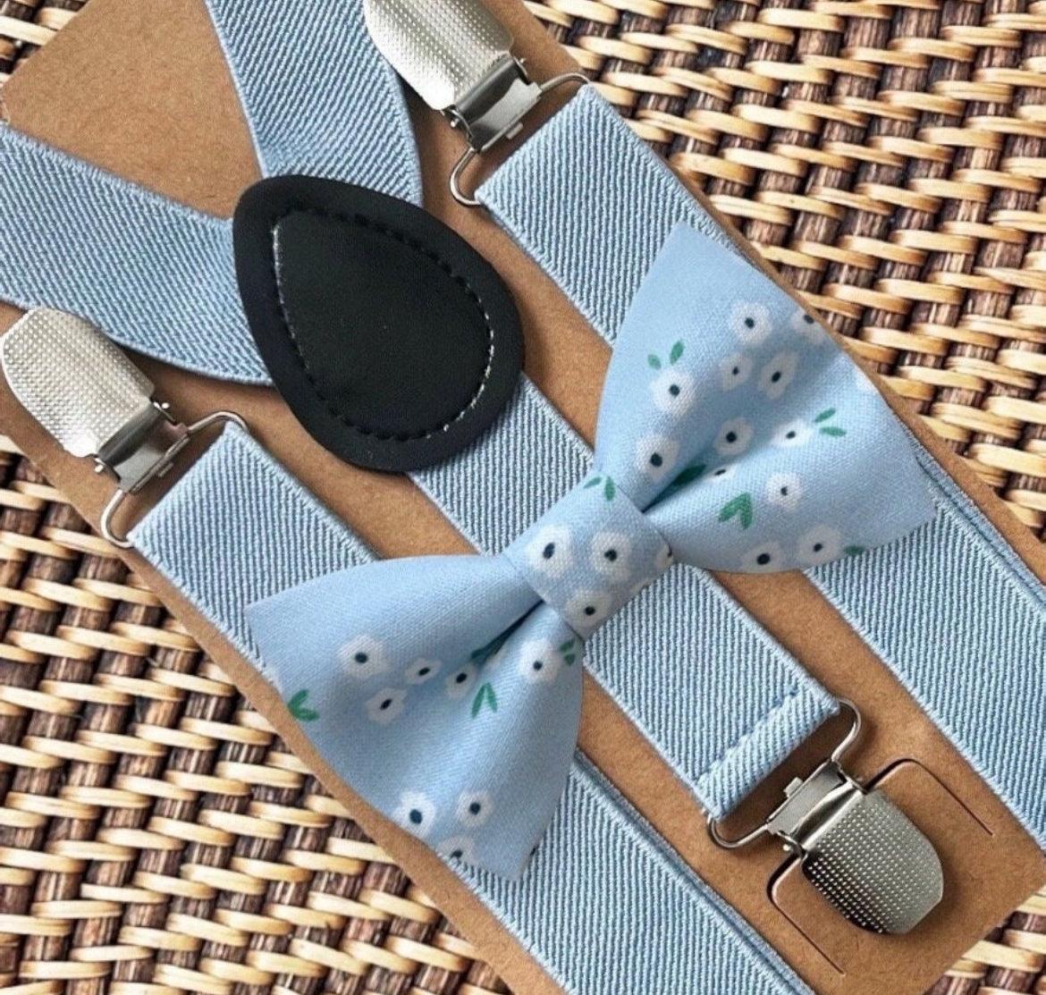 Dainty light blue daisy patterned bow tie with dusty blue suspenders and metal clips on a tan leather backdrop