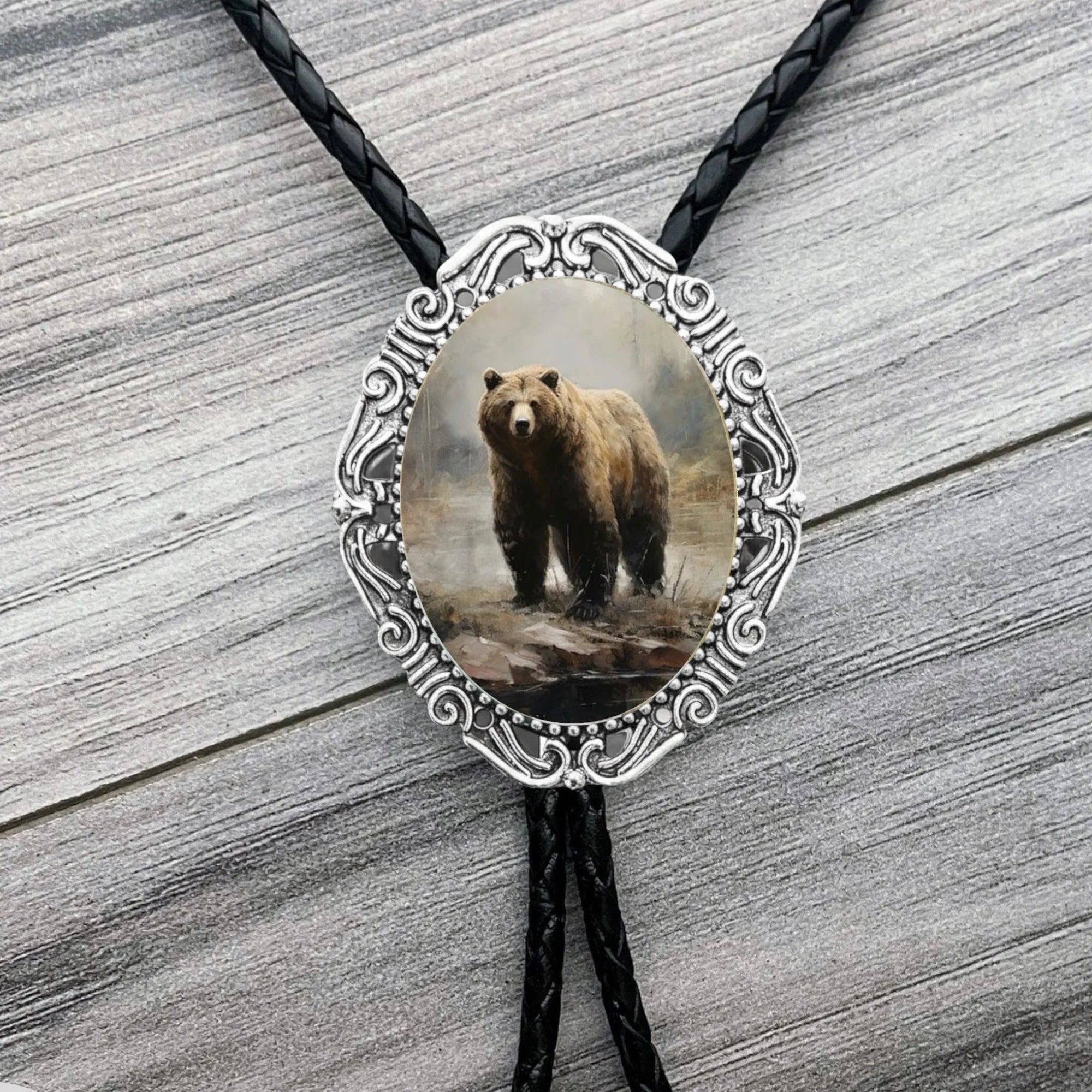 Infographic from The Bold Bow Tie titled Bolo Tie Features. Right: A vintage-style bolo tie with a blue and white cowboy riding a horse illustration inside an ornate bronze filigree frame on a black braided cord. Left: Lines connect the image to three checkmark features: Handmade, 39" Long Cord, and Pendant is 1.5" (L) x 1.25" (W). Bottom text reads Perfect Addition to Your Outfit.