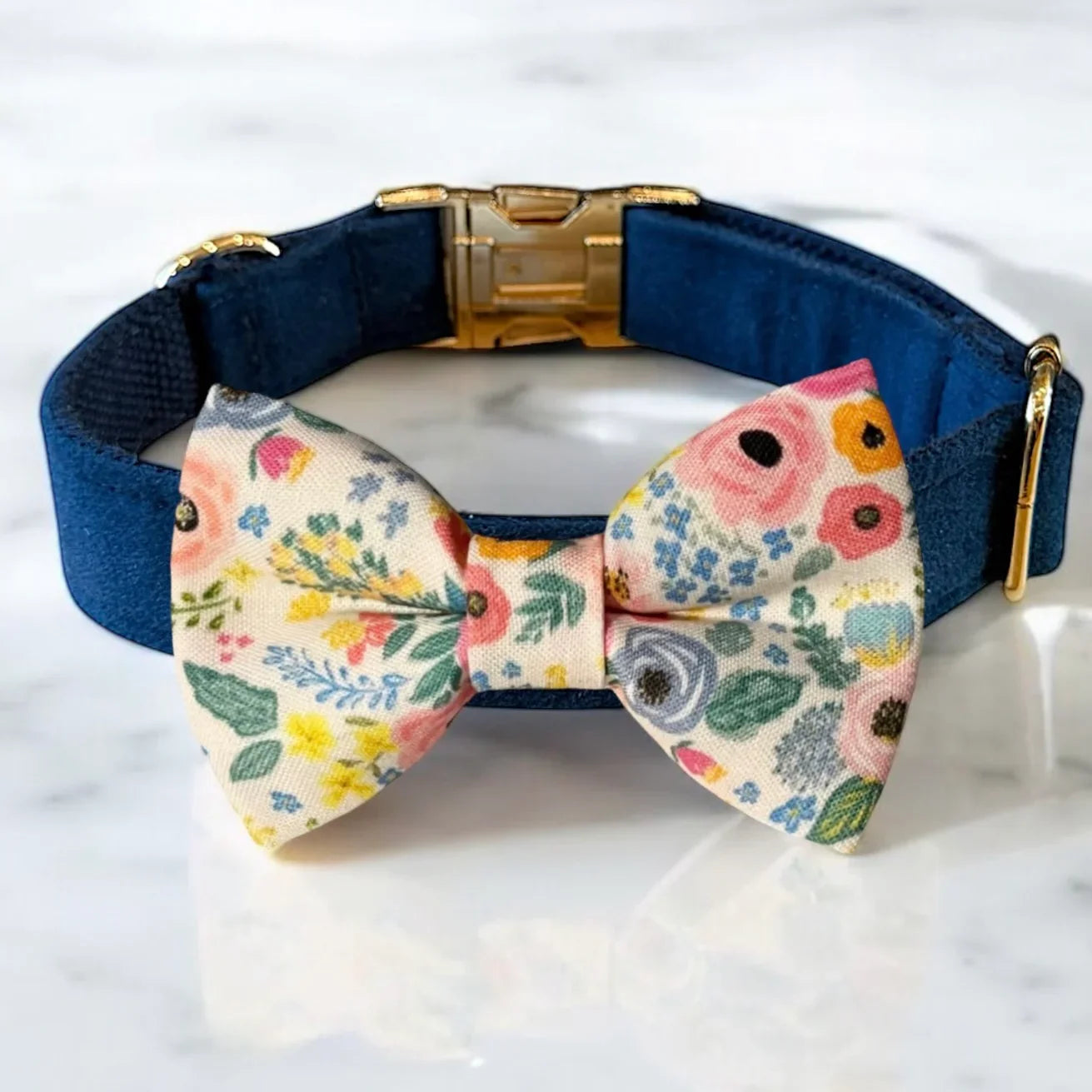 Navy blue velvet dog collar with a floral dog bow tie on a marble surface