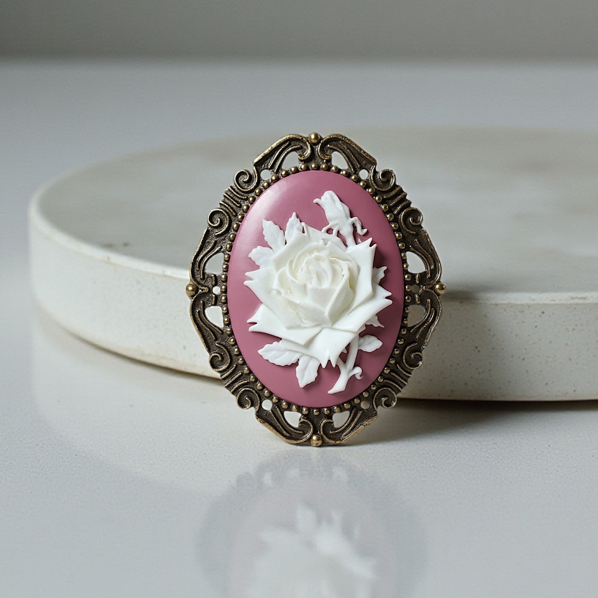 Decorative brooch with a white rose design on a pink background, set against a light gray background.