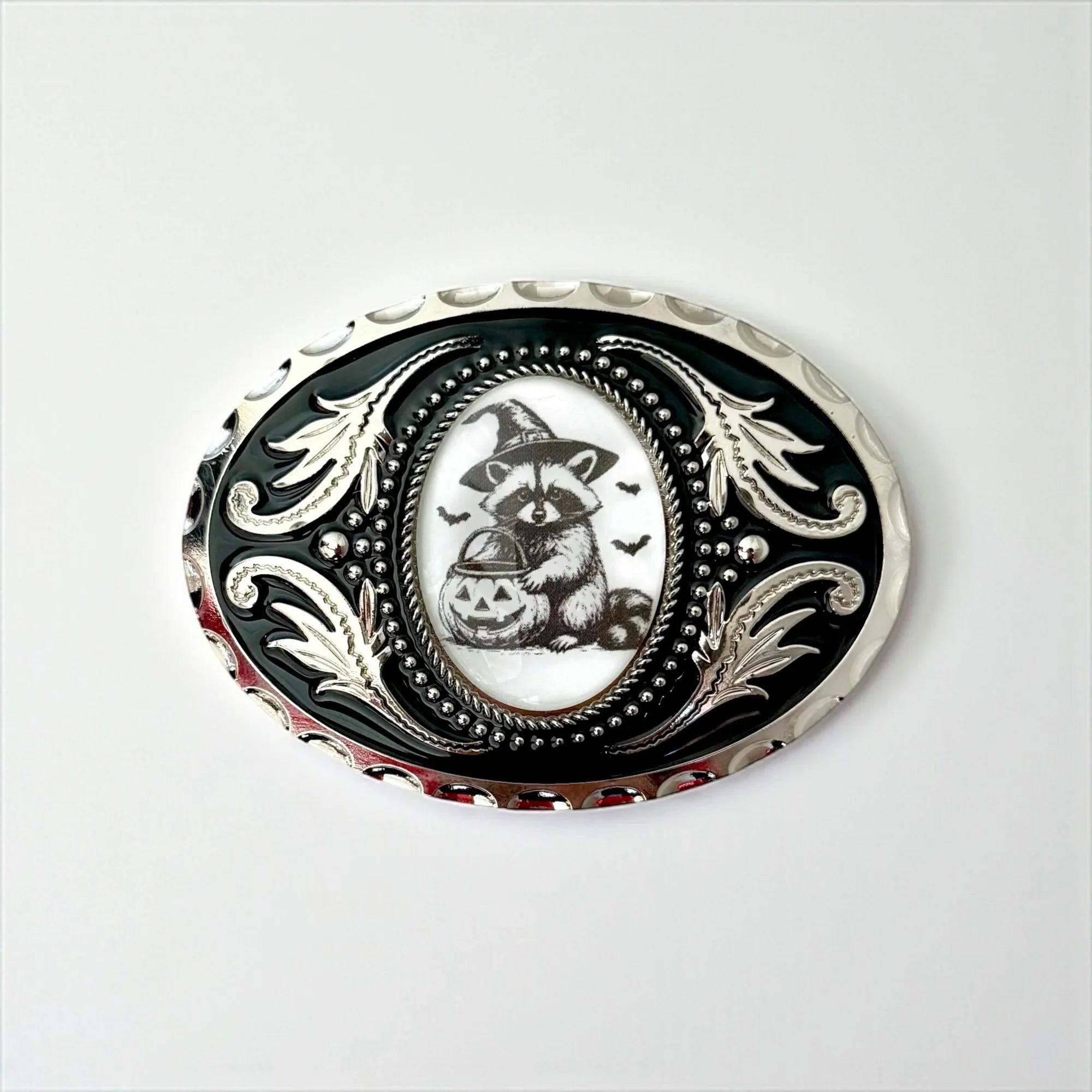 Halloween Belt buckle with raccoon design and decorative border on a white background