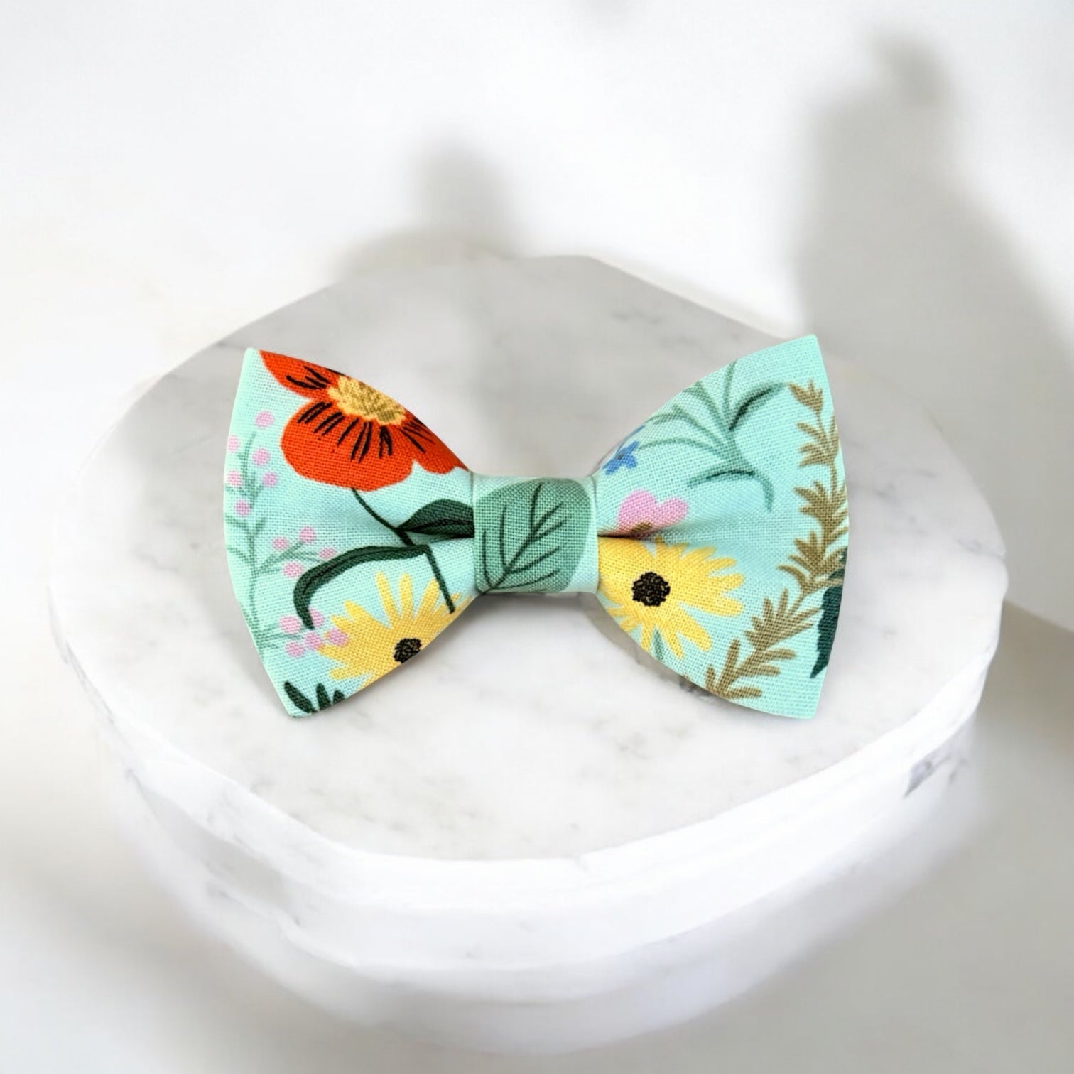 Blue and green floral men’s bow tie for weddings, groomsmen or ring bearers on a marble pedestal.