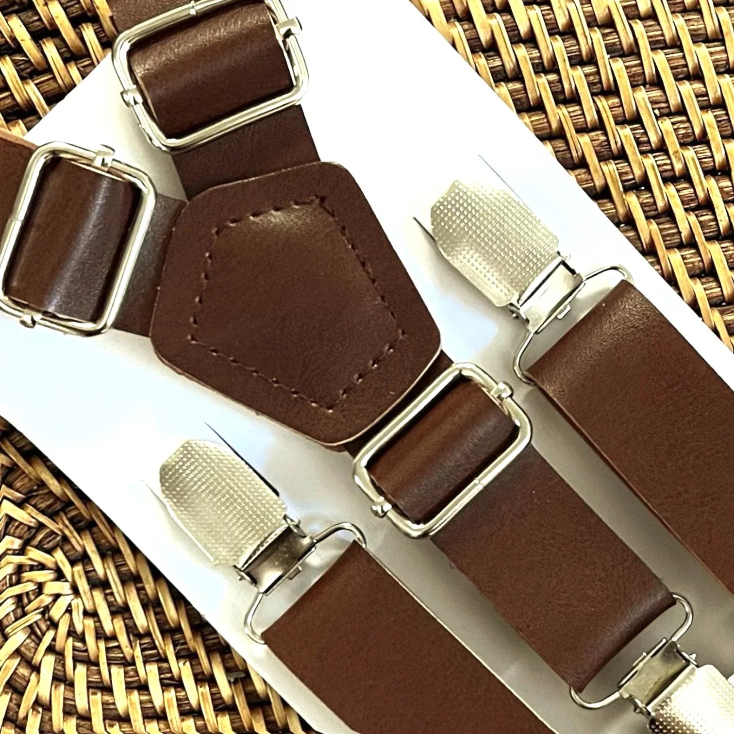 Dark brown vegan leather suspenders with silver buckles laid on a white display card