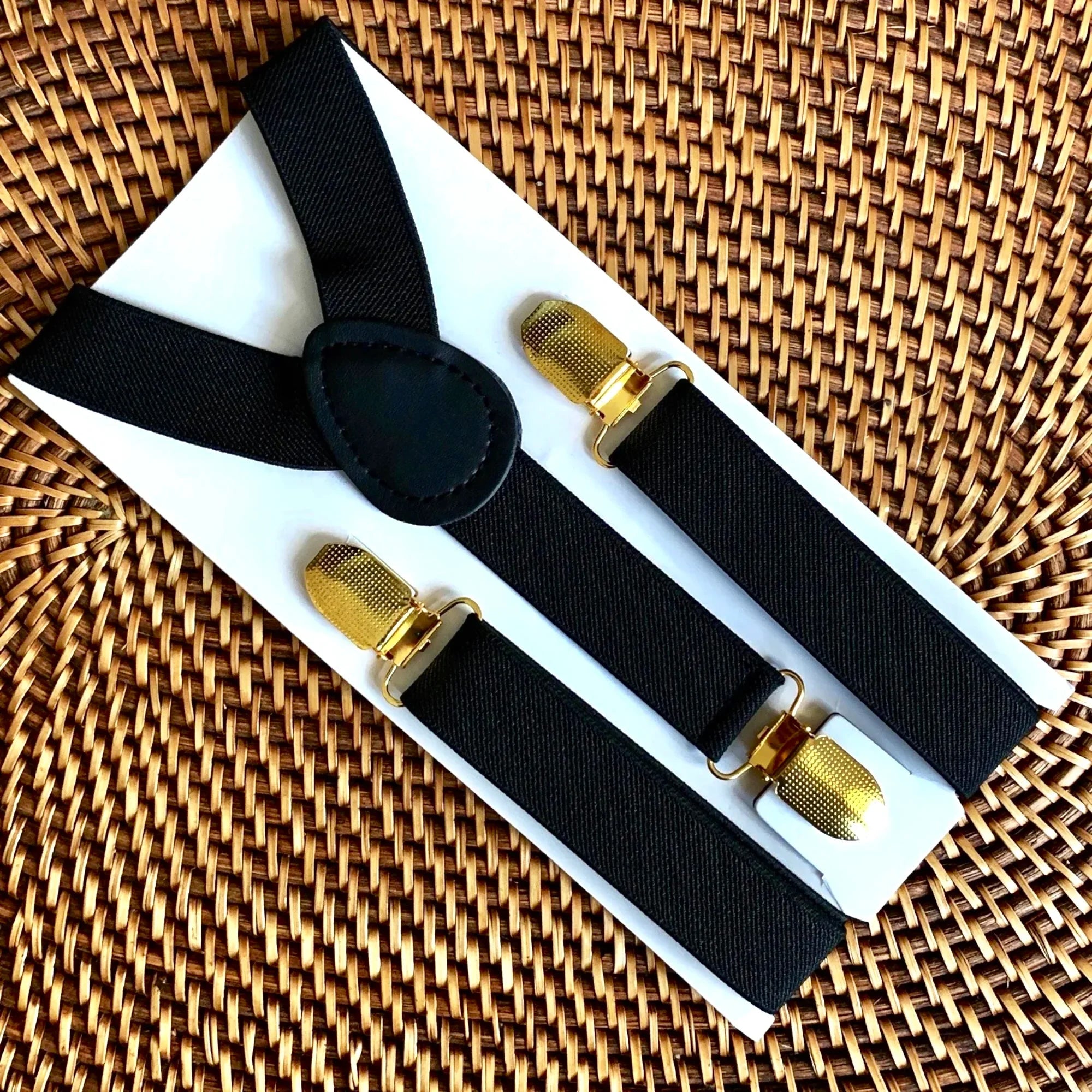 Black suspenders with gold clips on a white box against a woven background