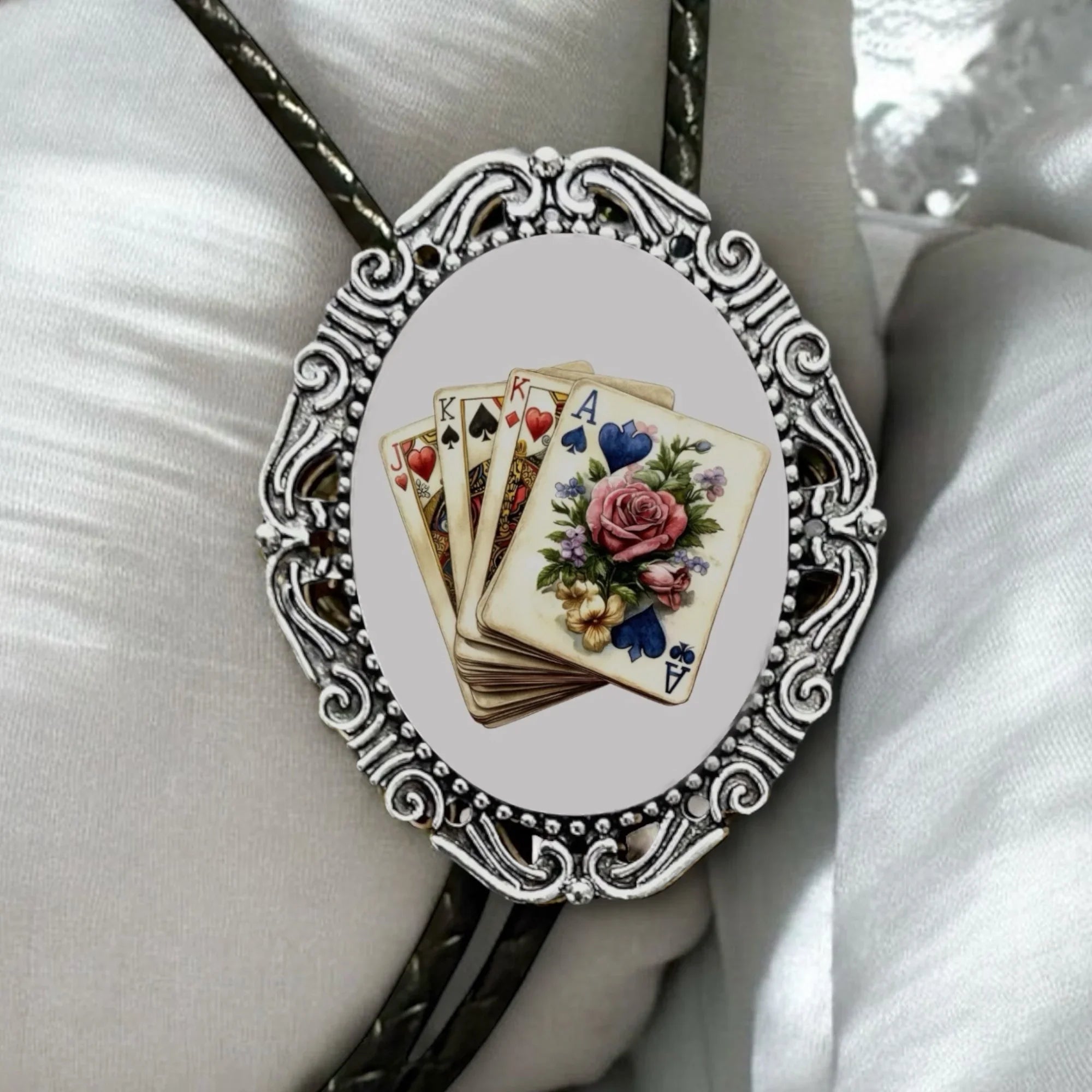 Infographic from The Bold Bow Tie titled Bolo Tie Features. Right: A vintage-style bolo tie with a blue and white cowboy riding a horse illustration inside an ornate bronze filigree frame on a black braided cord. Left: Lines connect the image to three checkmark features: Handmade, 39" Long Cord, and Pendant is 1.5" (L) x 1.25" (W). Bottom text reads Perfect Addition to Your Outfit.
