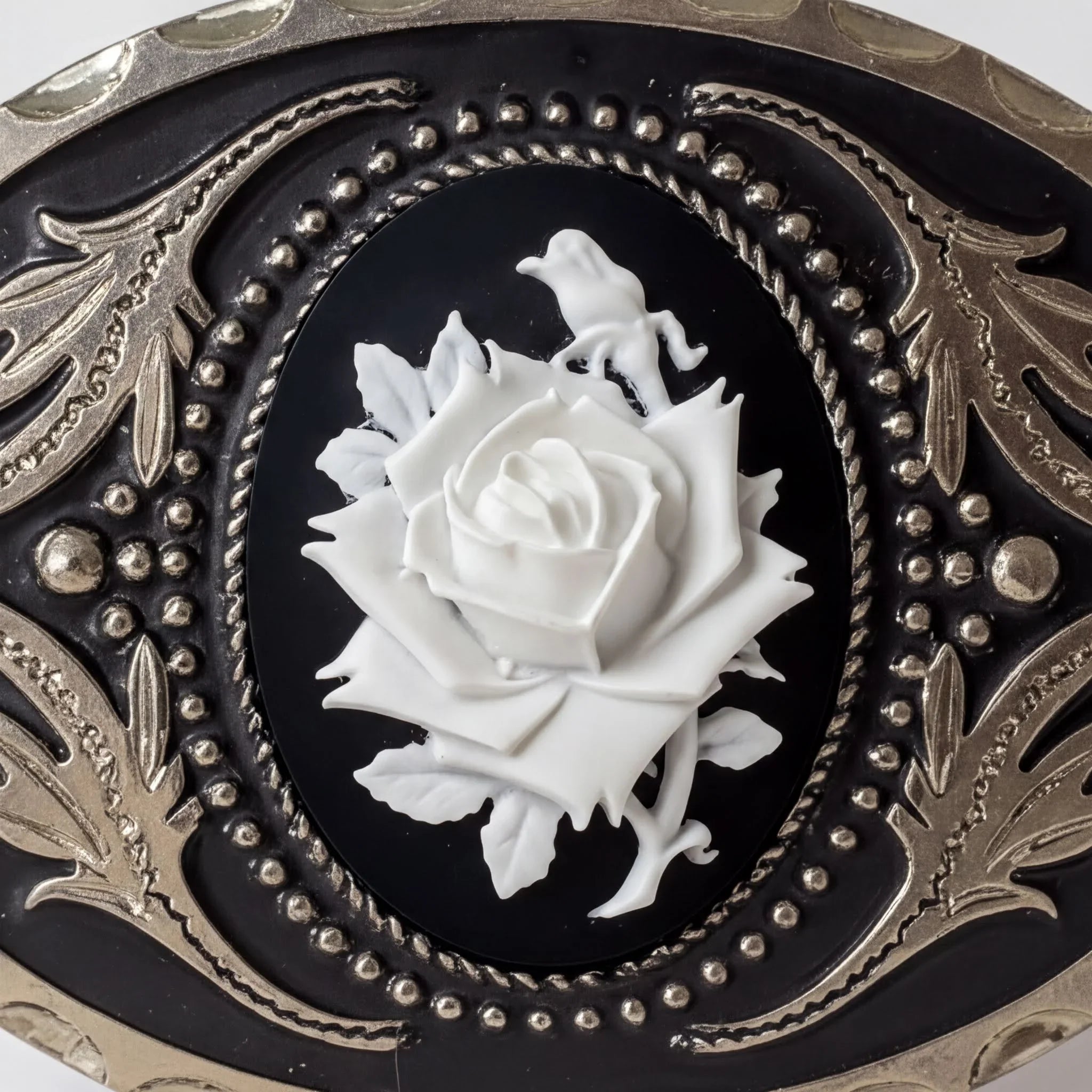 a close-up view of a decorative piece with a black background and a white rose as the central element. The rose is surrounded by intricate metalwork and patterns, creating a visually striking and elegant design.