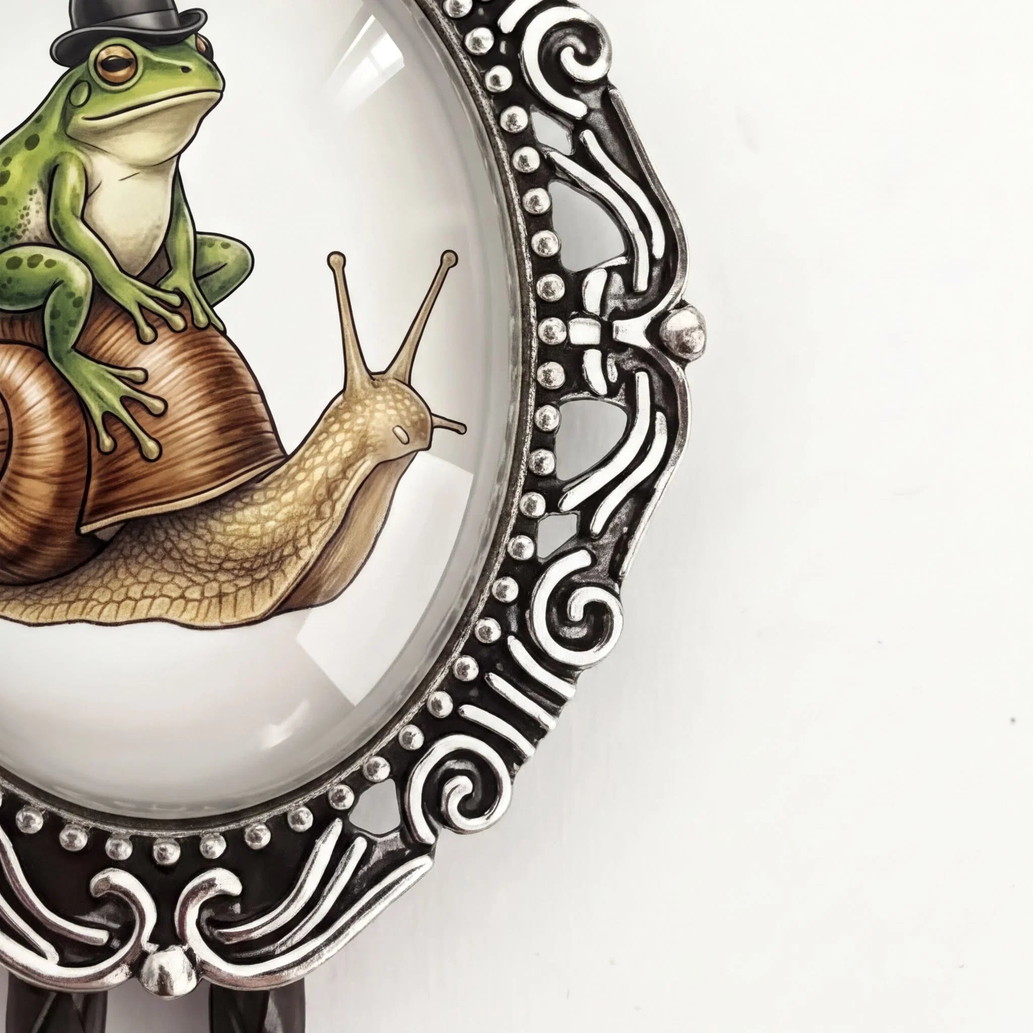 A decorative metal frame with a glass pane containing an illustration of a frog sitting on a snail.