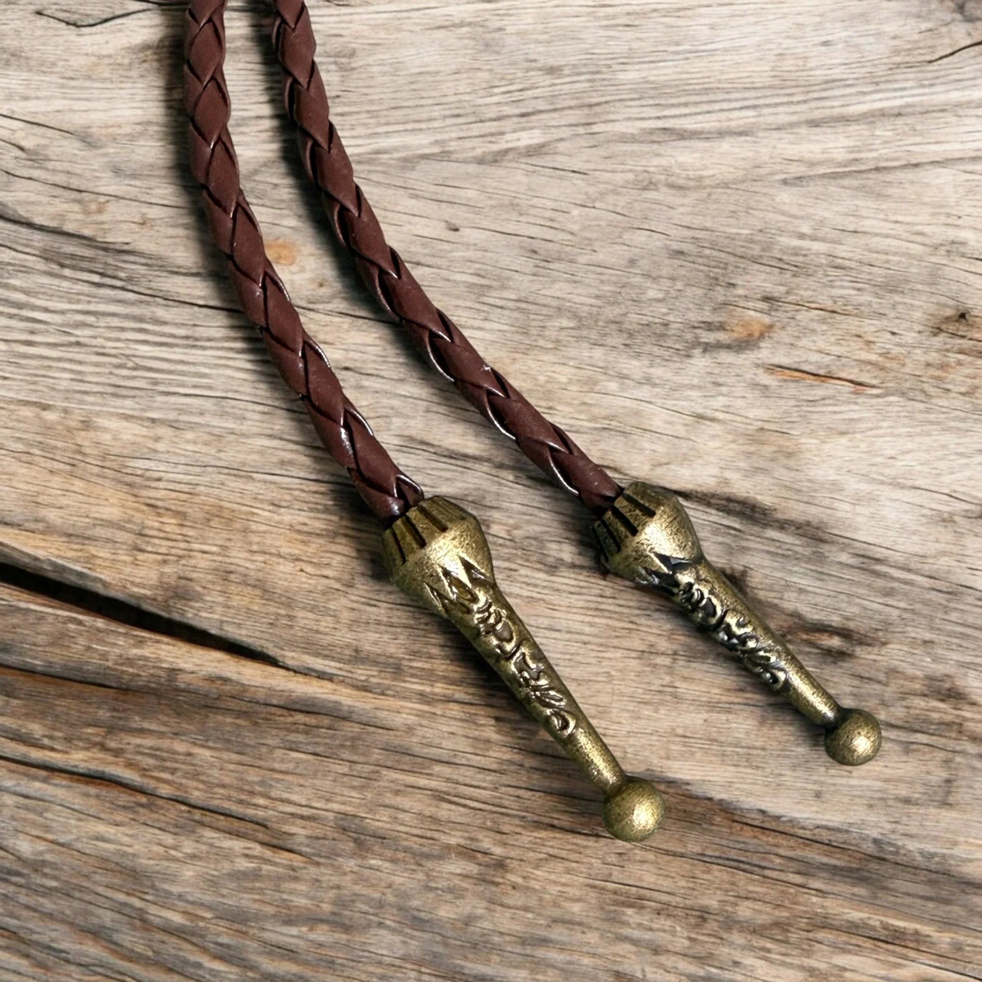Braided leather bolo tassels with brass ends on a wooden surface