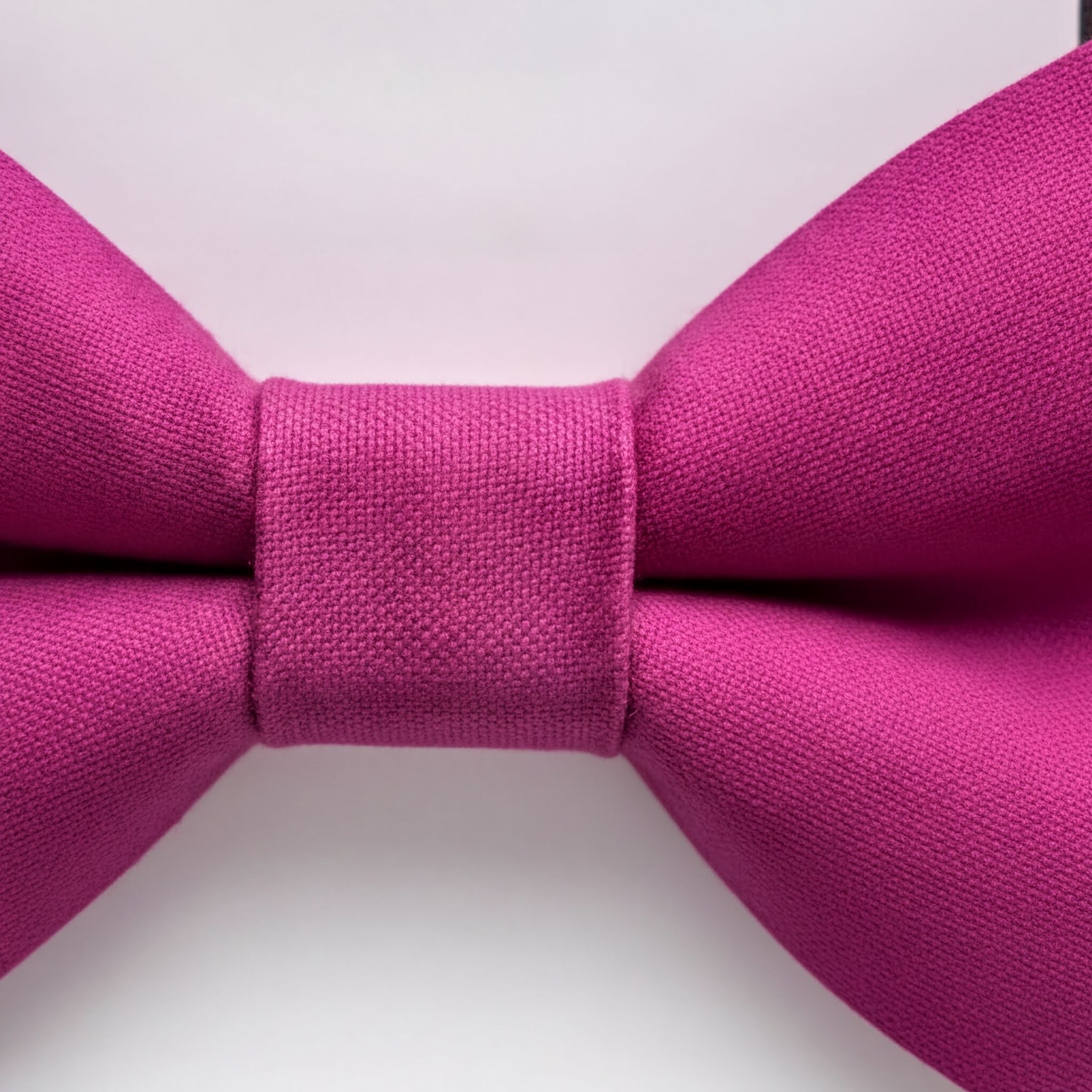 A close-up view of a vibrant pink bow tie against a plain white background.