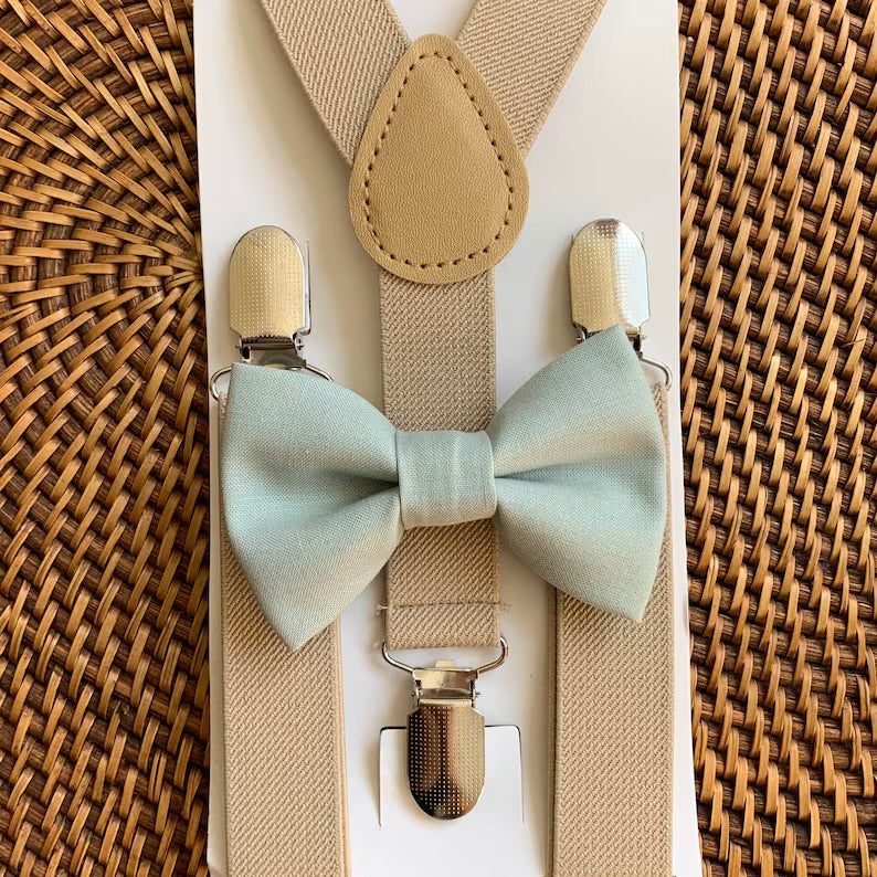 Sage Green Bow Tie & Tan Suspenders Set for wedding groomsmen, groom and ring bearers on a brown woven tray.