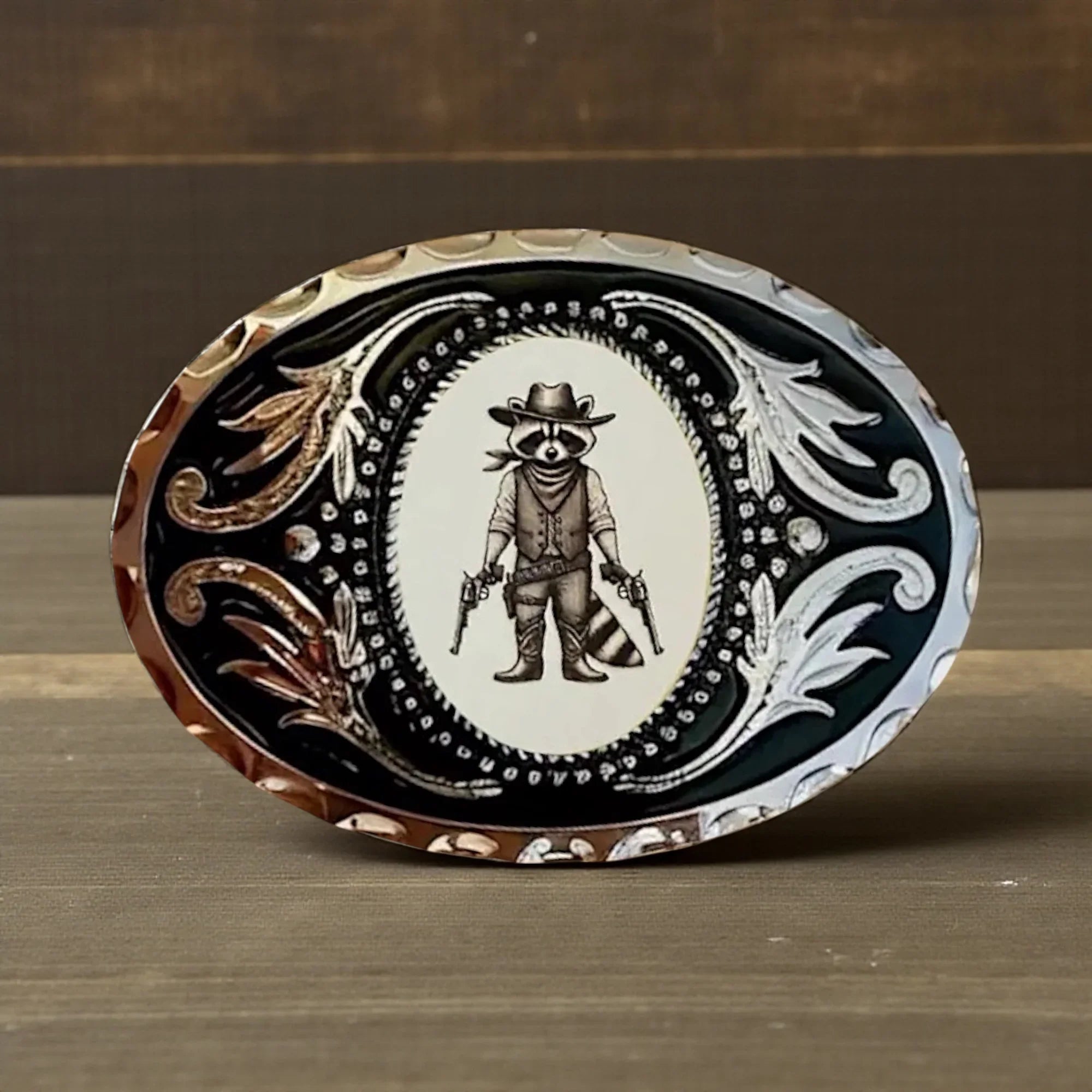 Western belt buckle with a raccoon in cowboy attire on a wooden surface