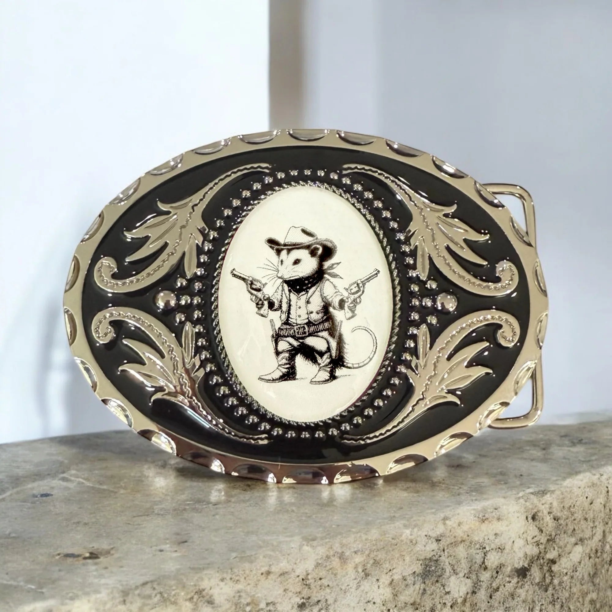 Decorative belt buckle with a cowboy opossum design on a stone surface.