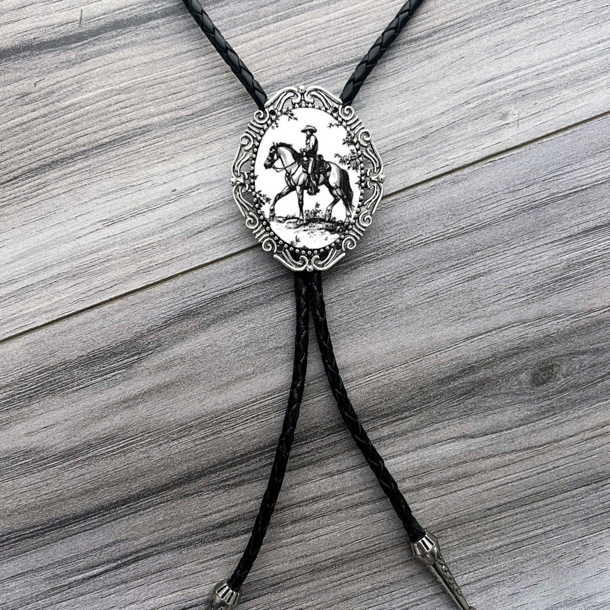 Bolo tie with a decorative pendant featuring a horse and rider on a wooden surface