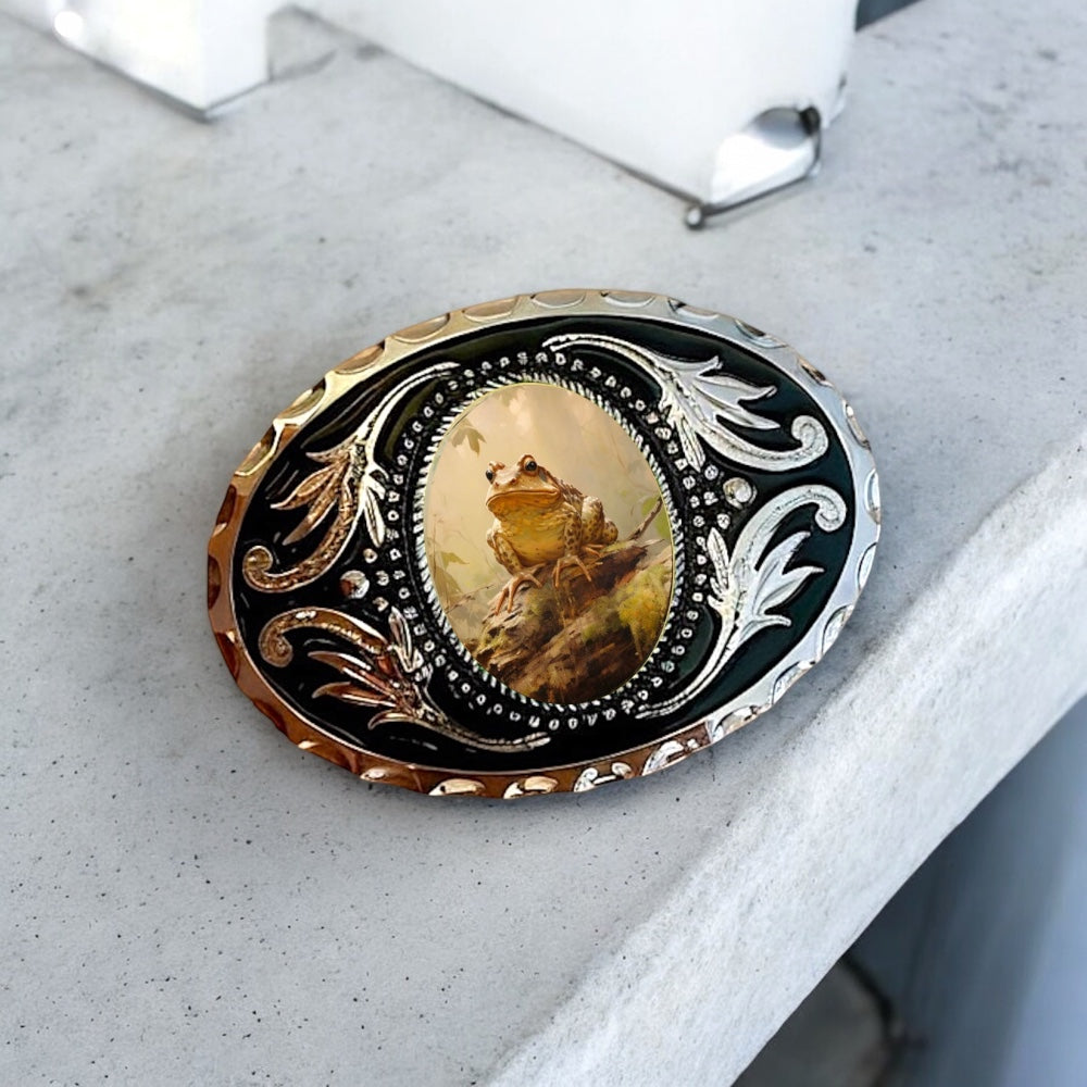 Frog belt buckle with intricate design on a concrete surface
