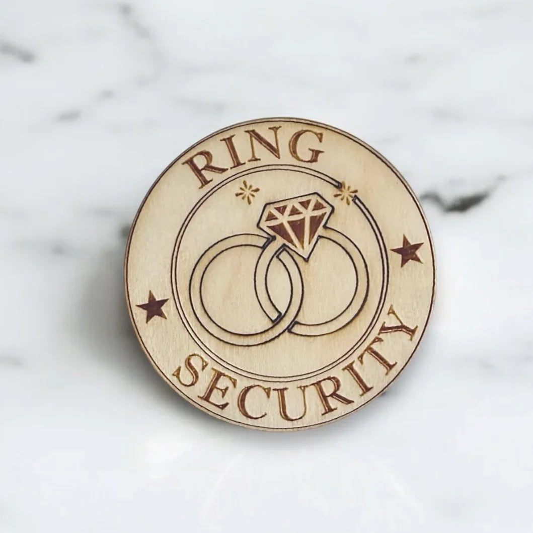 Round wooden badge engraved with RING SECURITY and two interlocking rings between decorative stars.