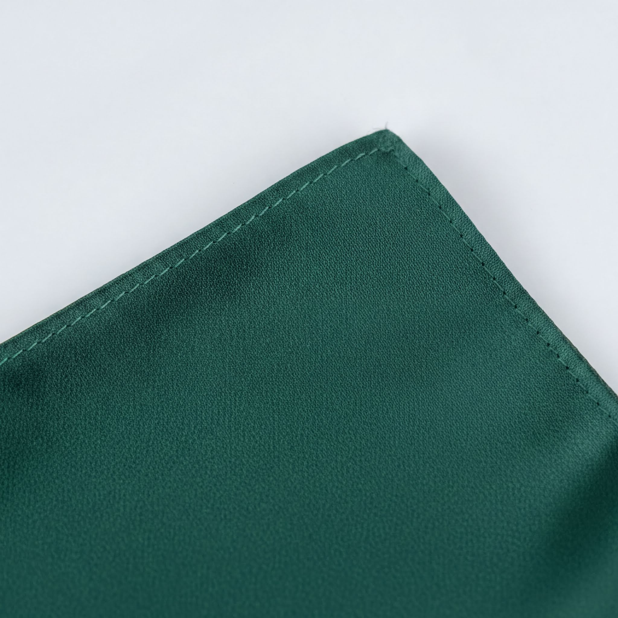 A close-up view of a dark green fabric, possibly a napkin or cloth, with a small, neatly sewn seam running along the edge.