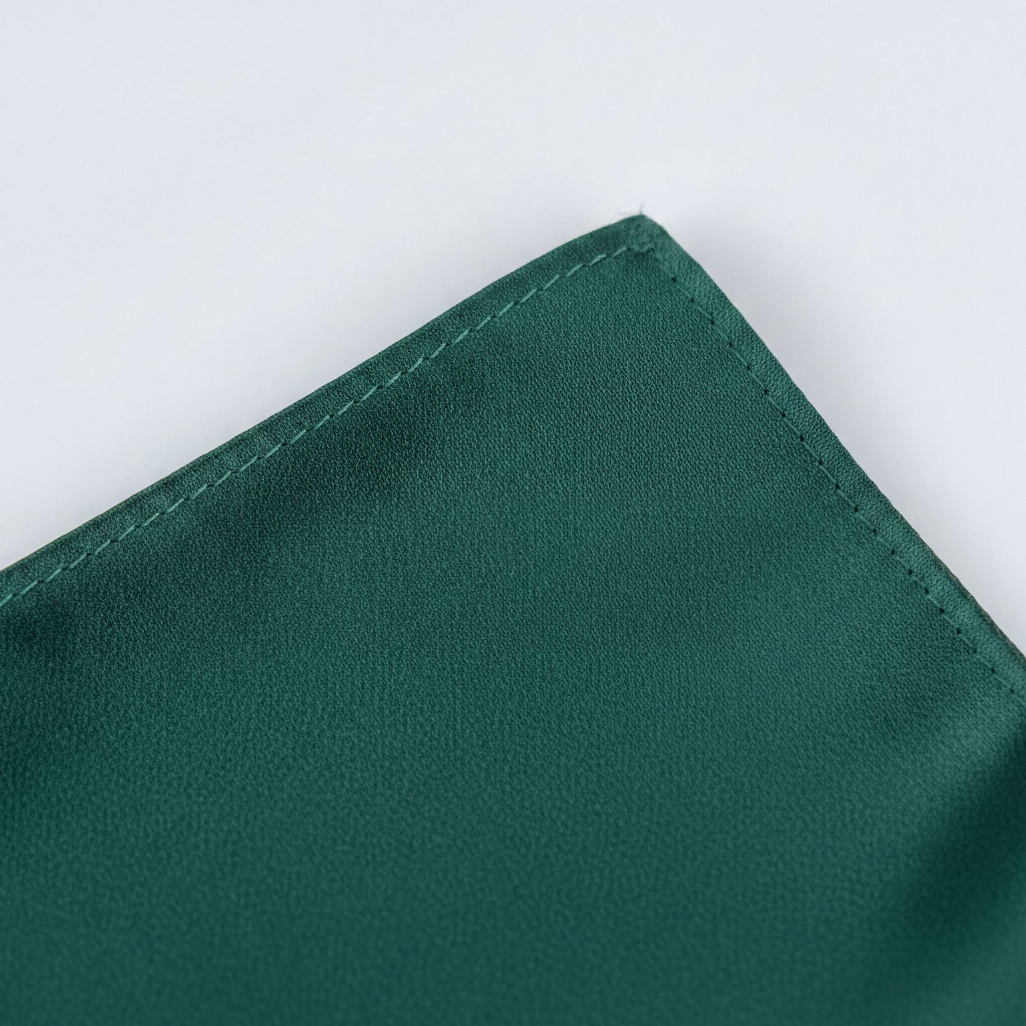 A close-up view of a dark green fabric, possibly a napkin or cloth, with a small, neatly sewn seam running along the edge.