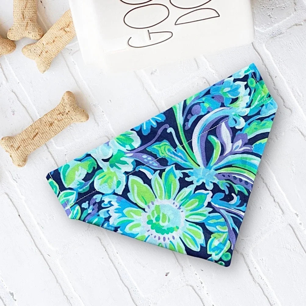 Blue and purple floral dog bandana laid flat on a white textured surface.