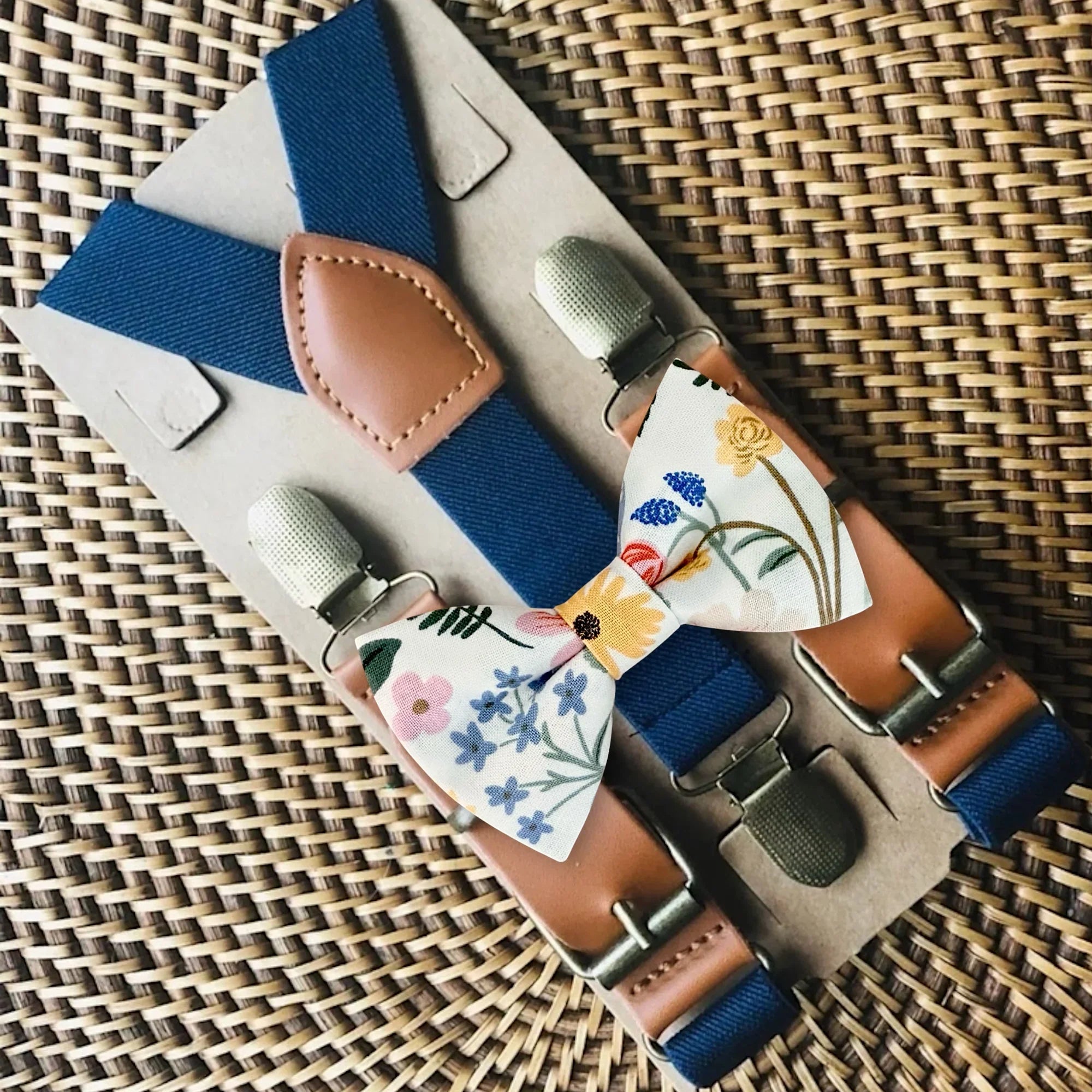 Ivory bow tie and suspenders with floral print and navy suspenders for ring bearers and groomsmen in wedding.