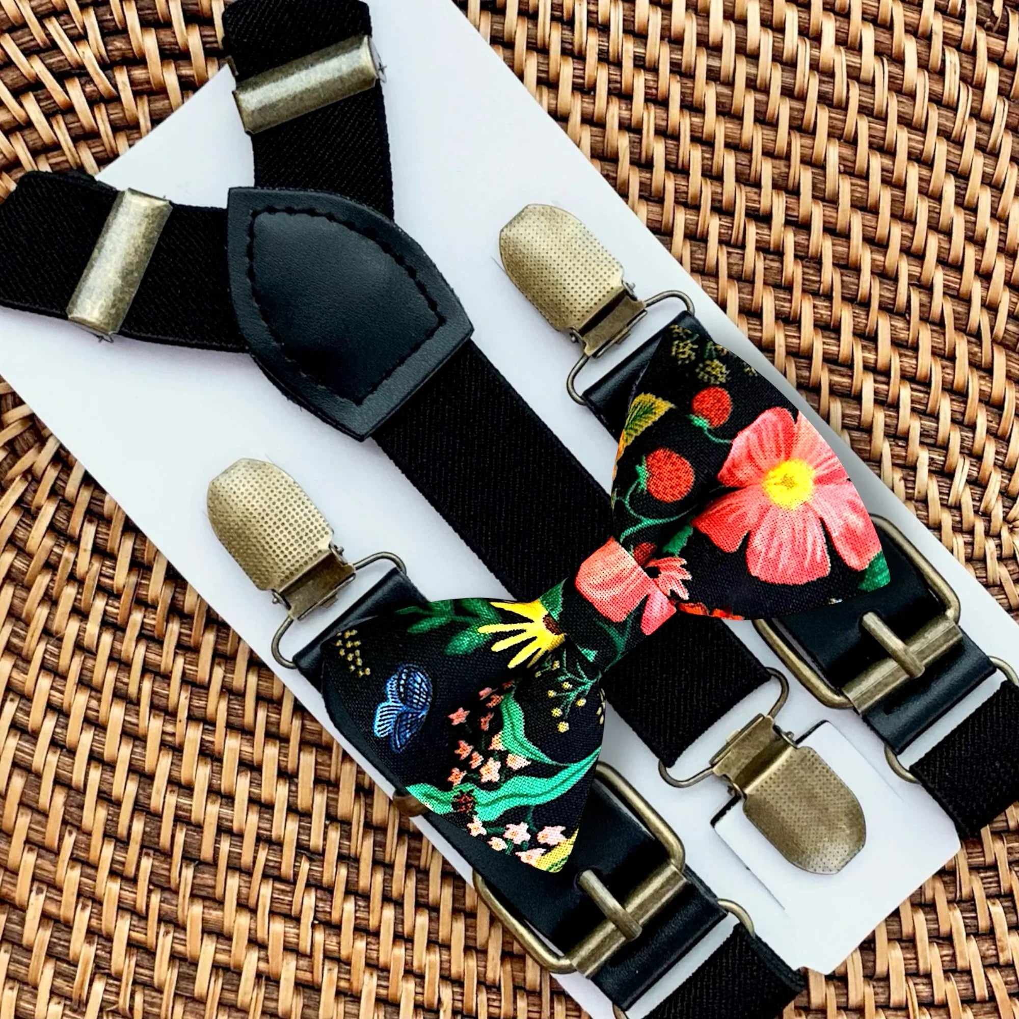 Floral bow tie and black suspenders with gold clasps on a woven surface