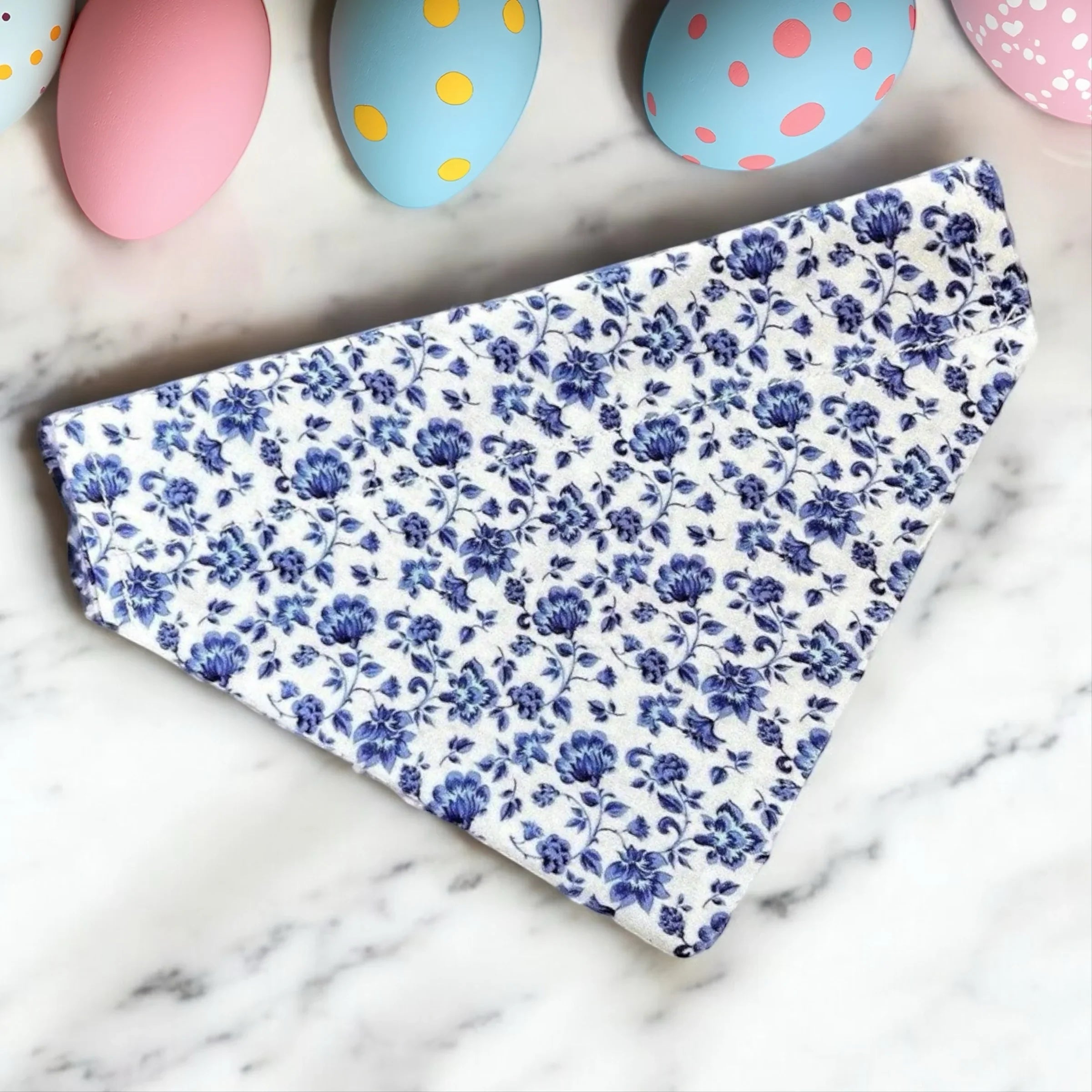 Blue floral fabric on a marble surface with colorful Easter eggs in the background