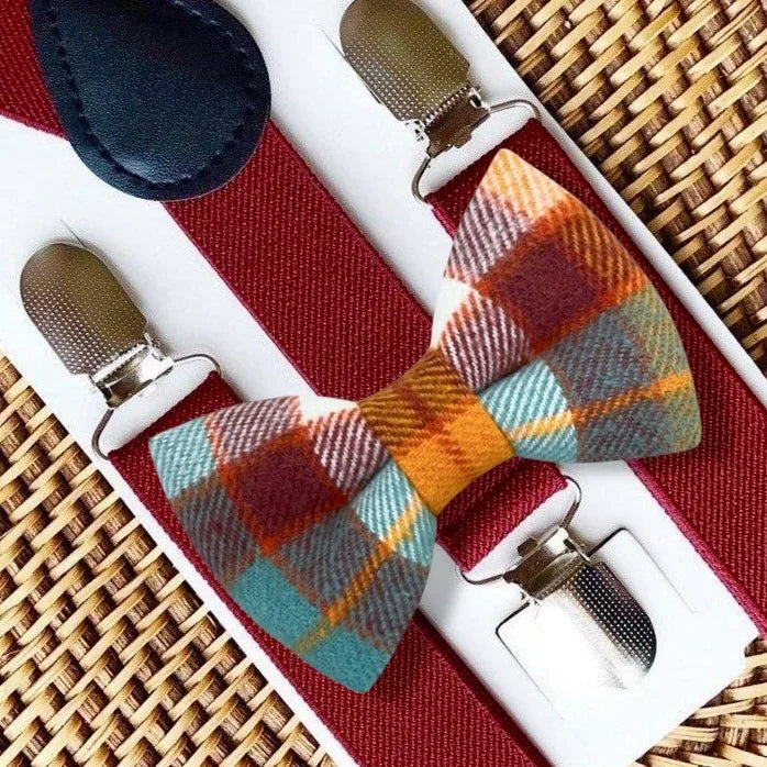 Fall plaid bow tie with burgundy suspenders laid on a white display card over a woven surface.