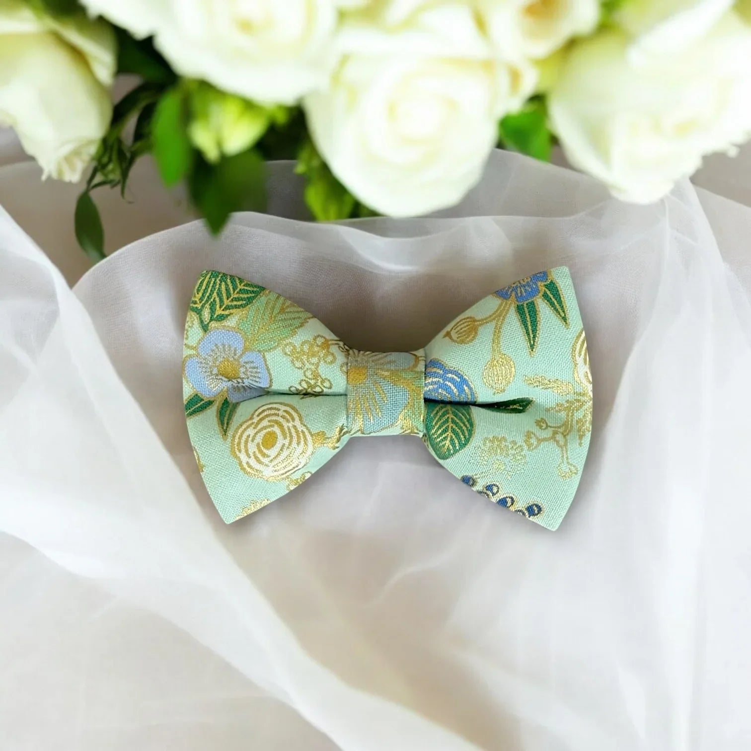Sage green bow tie on a white fabric with flowers in the background