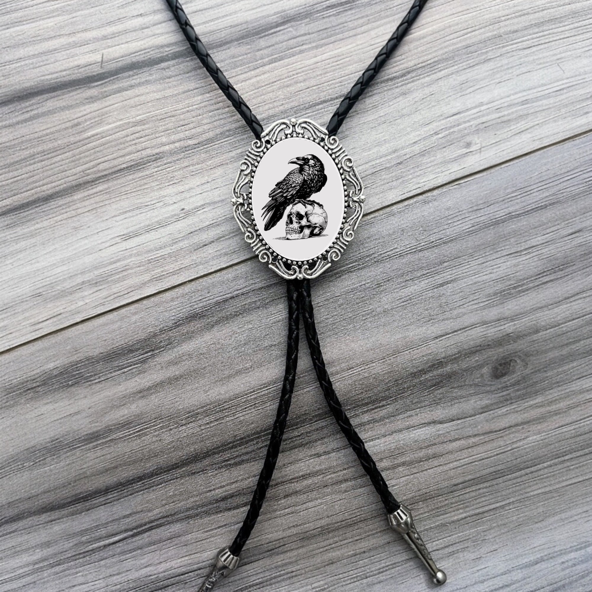 Bolo tie with a decorative pendant featuring a raven design on a wooden surface