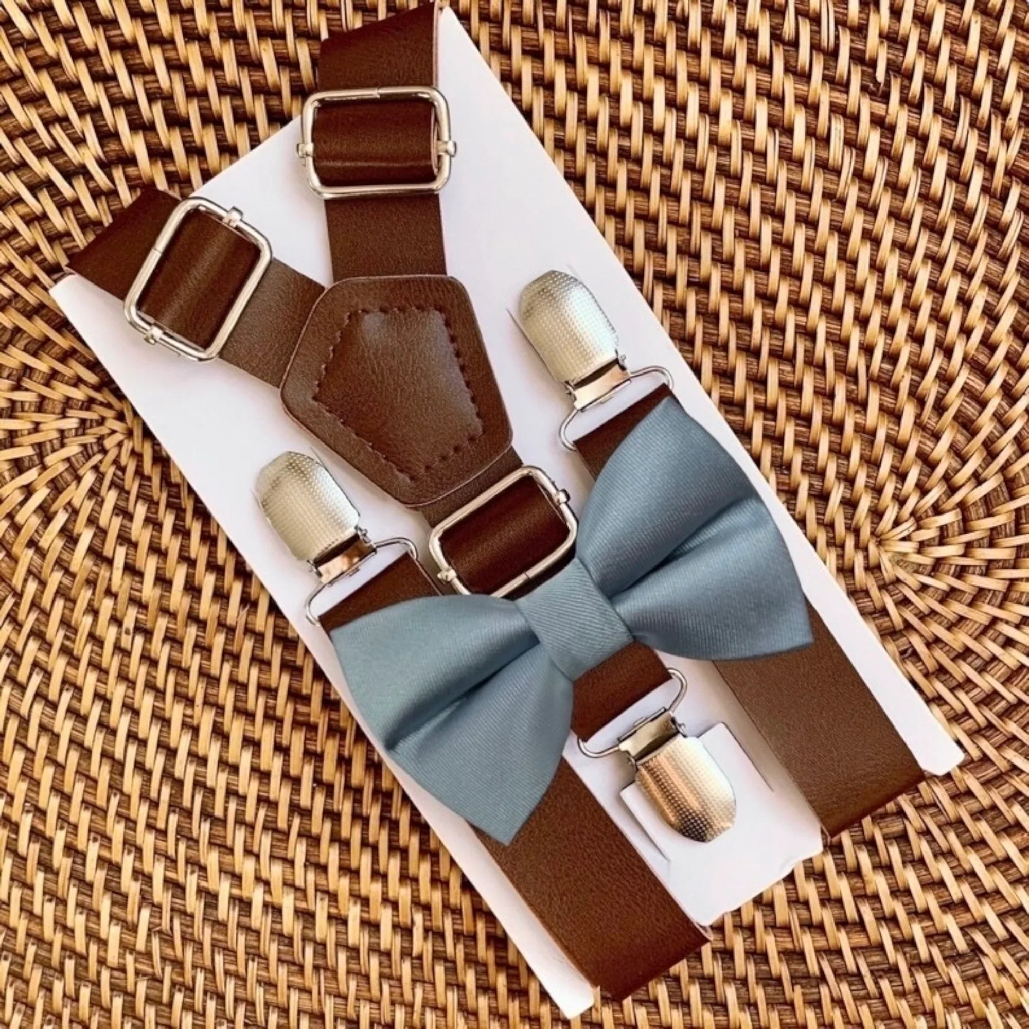 Dusty blue satin bow tie with brown vegan leather suspenders on a white display card