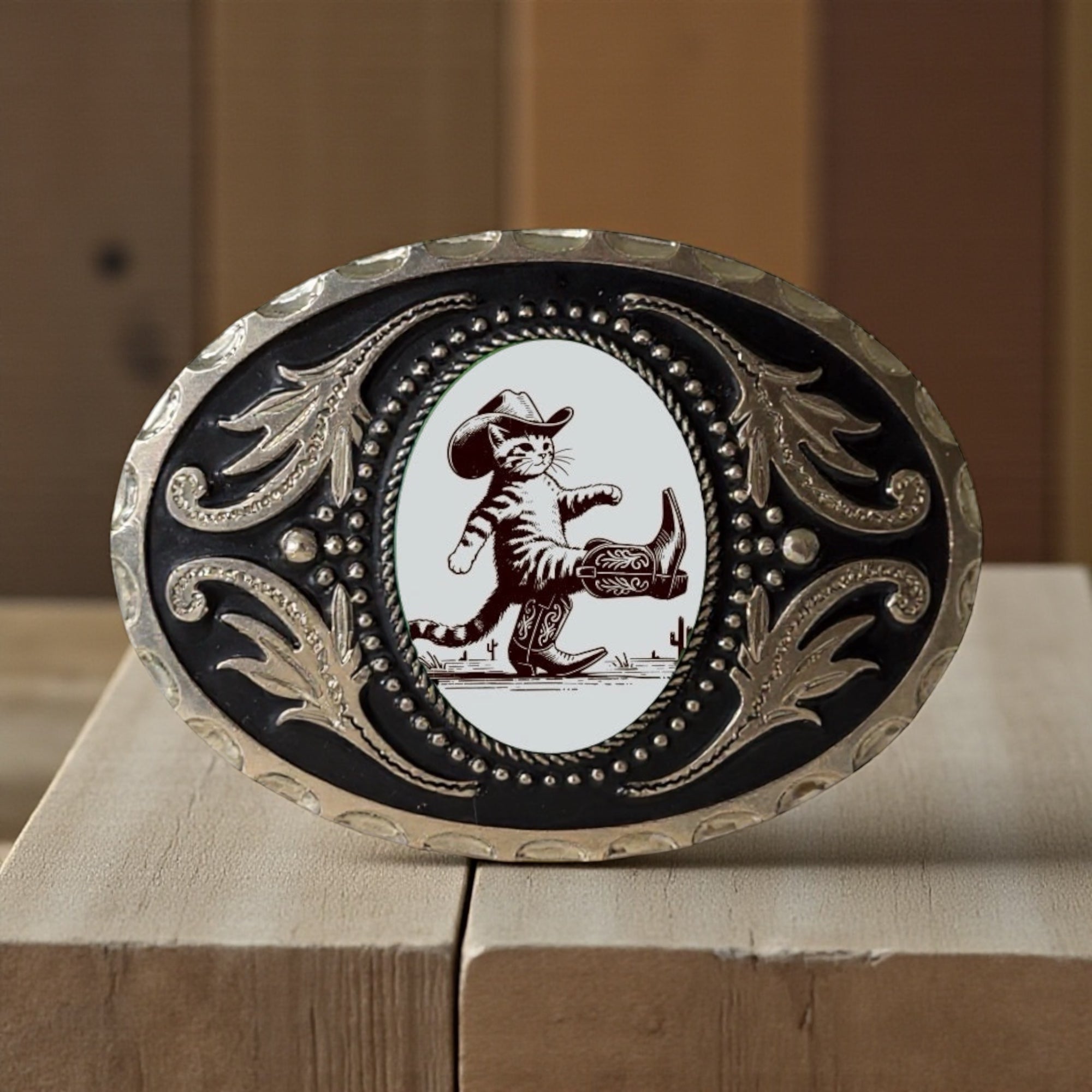 Decorative belt buckle with a cat in cowboy attire on a wooden surface