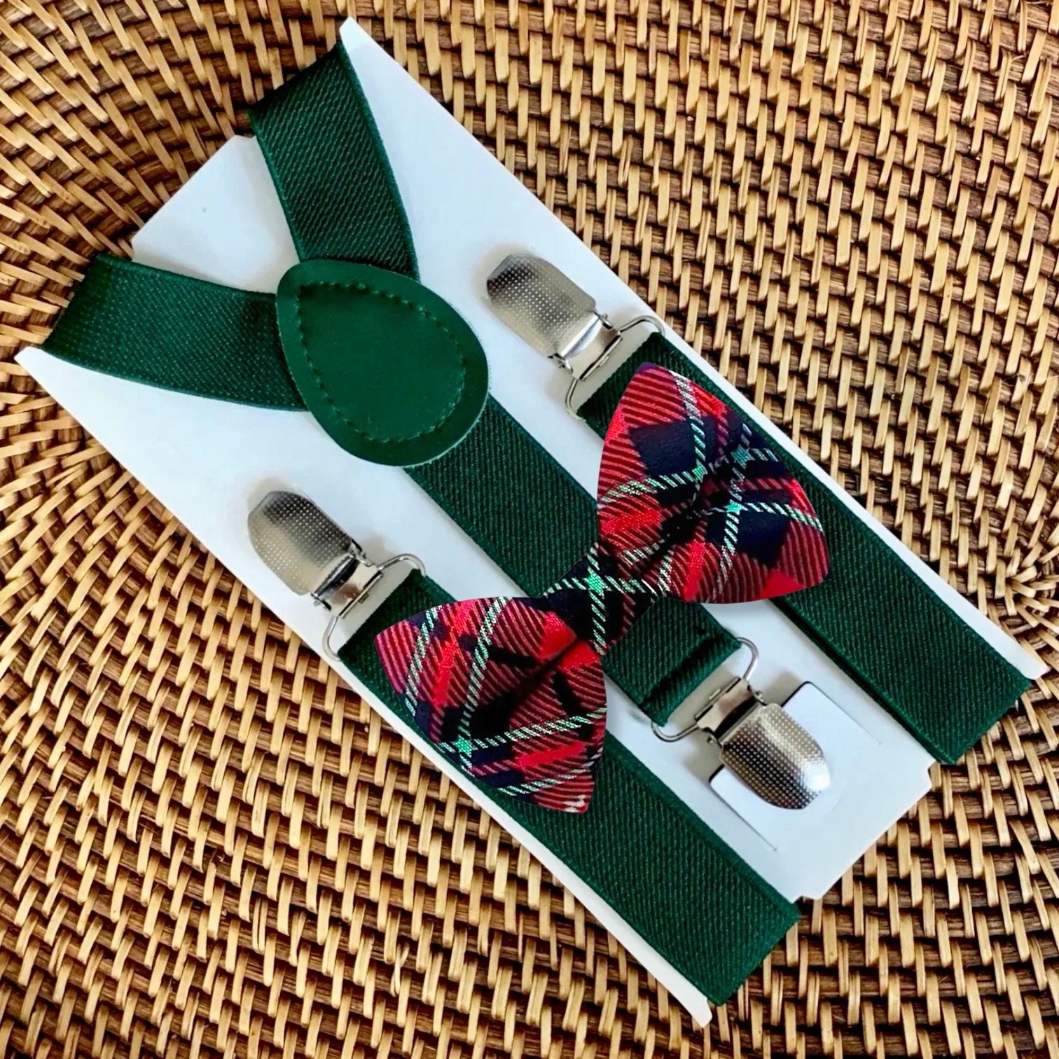 Red and green bow tie and suspenders on a woven tray.