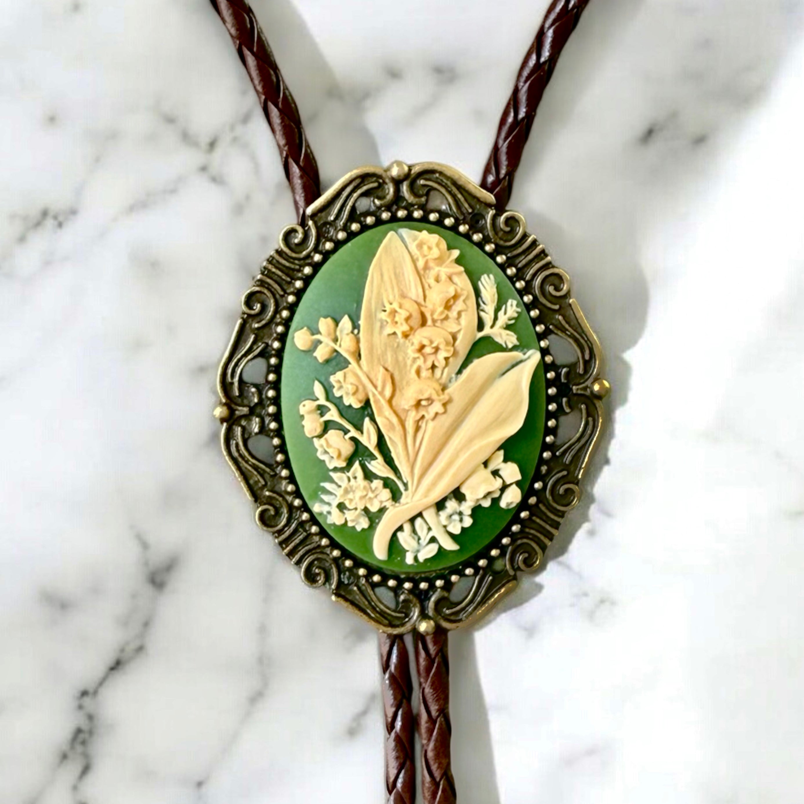 Green lily of the valley bolo tie with floral design on a marble background