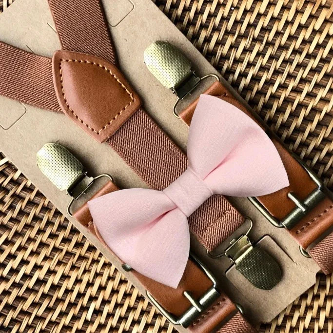 Blush pink bow tie with brown suspenders on a woven surface