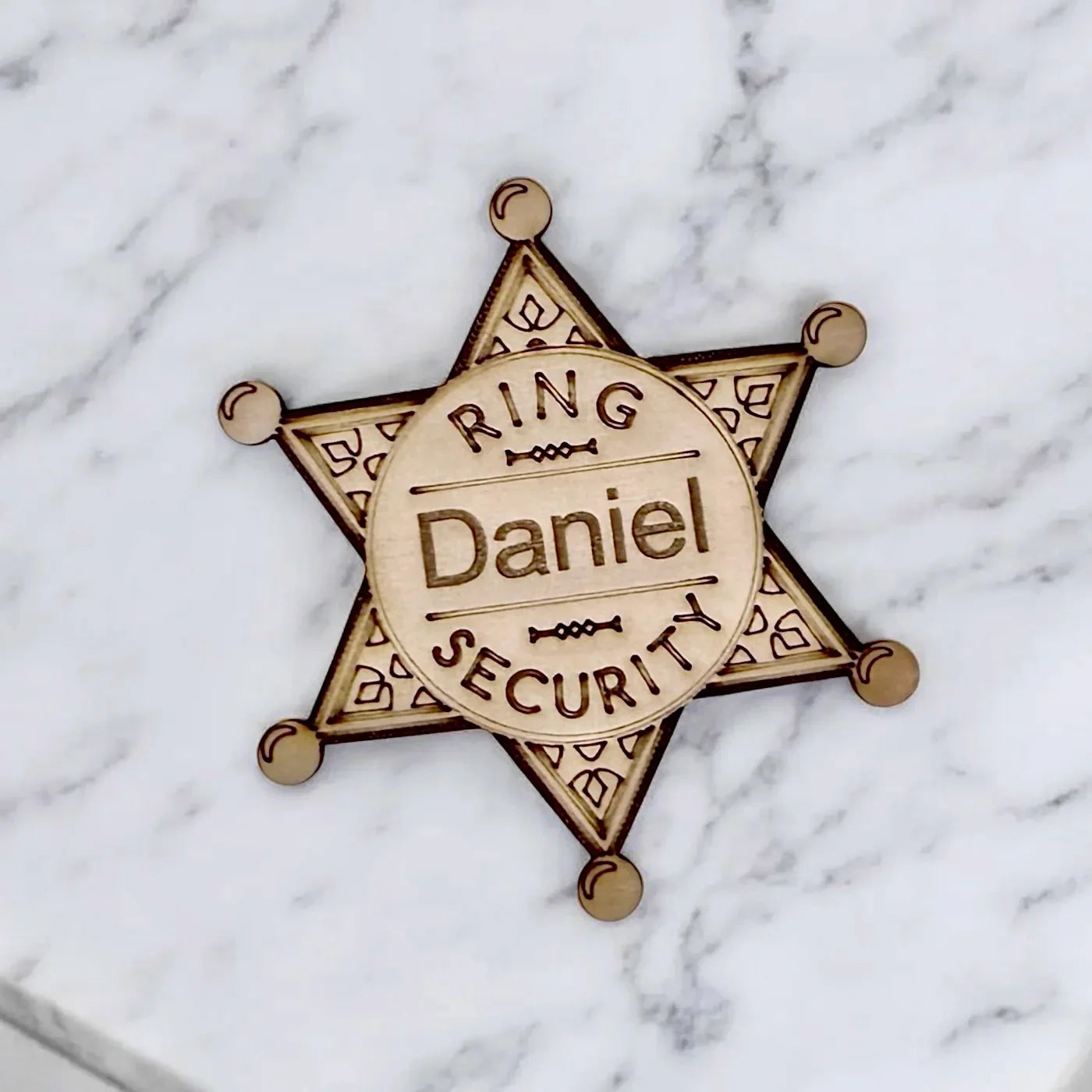 Close up of a wooden star shaped ring bearer badge featuring Daniel in the center