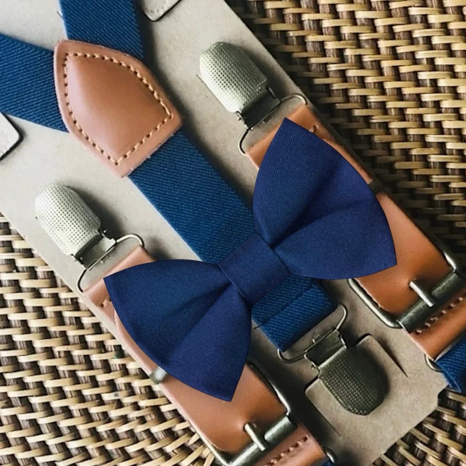 Navy blue bow tie and suspenders on a woven surface