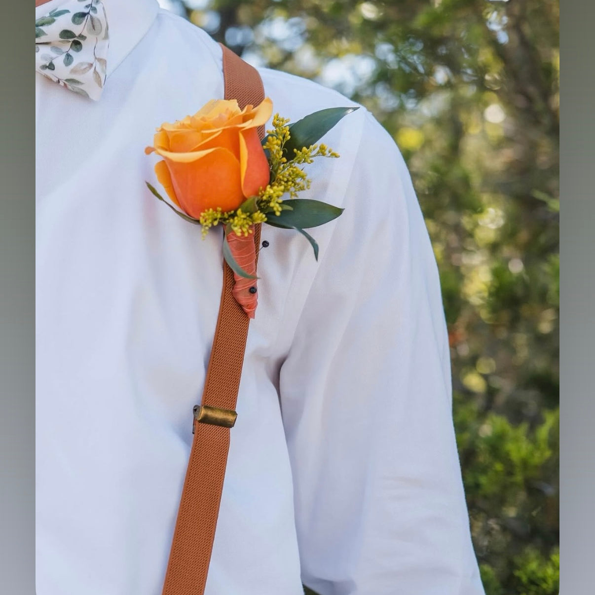 Sage floral bow tie and brown suspenders worn by a groomsman at a wedding.
