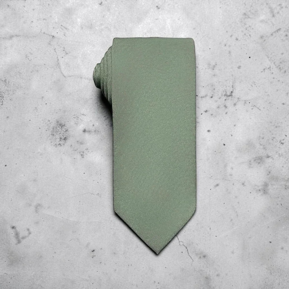 A sage green tie for men’s wedding necktie with a matching fabric neck loop, laid flat on a textured light gray concrete surface.