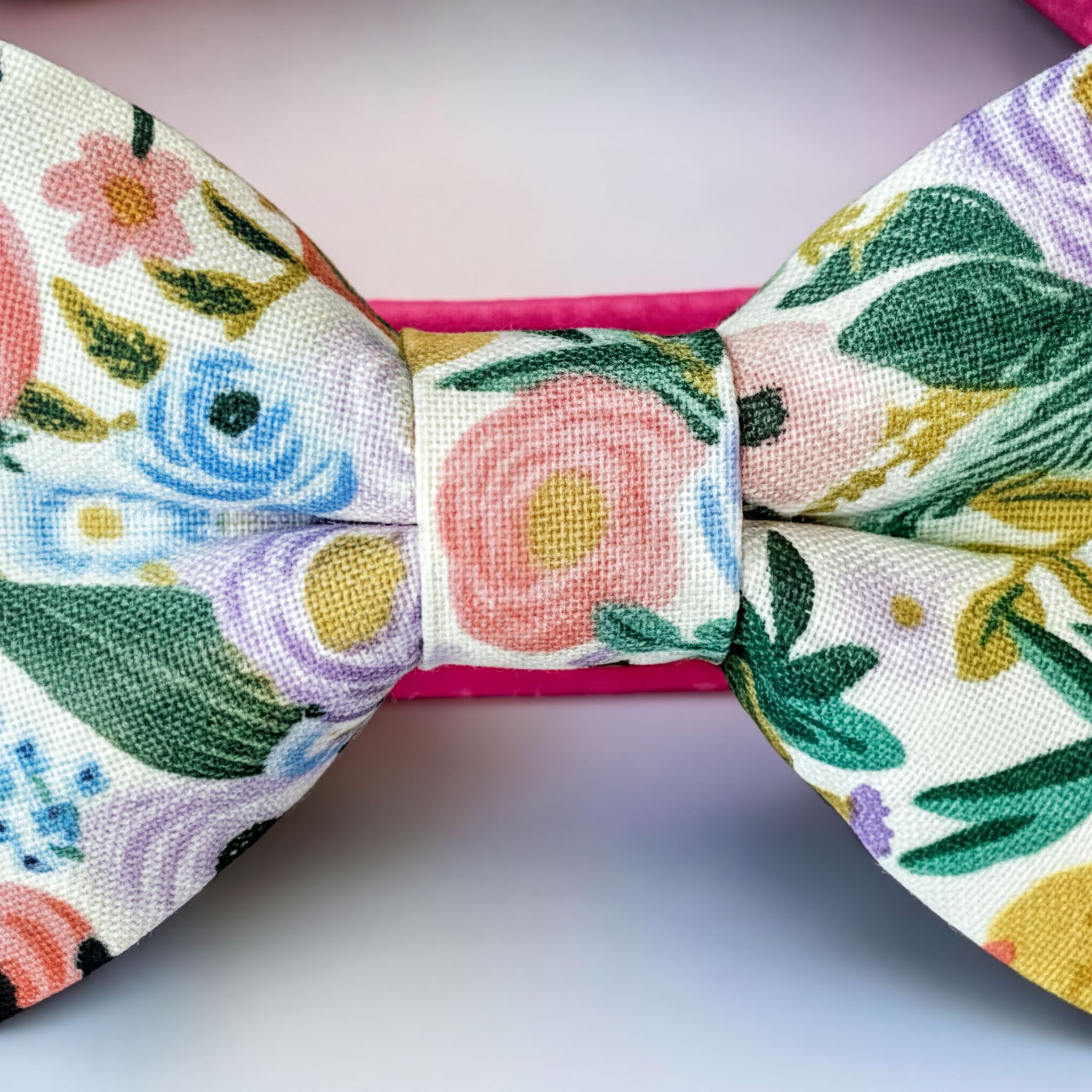 A close-up view of a colorful dog bow tie with a floral pattern, featuring a pink and green floral design.
