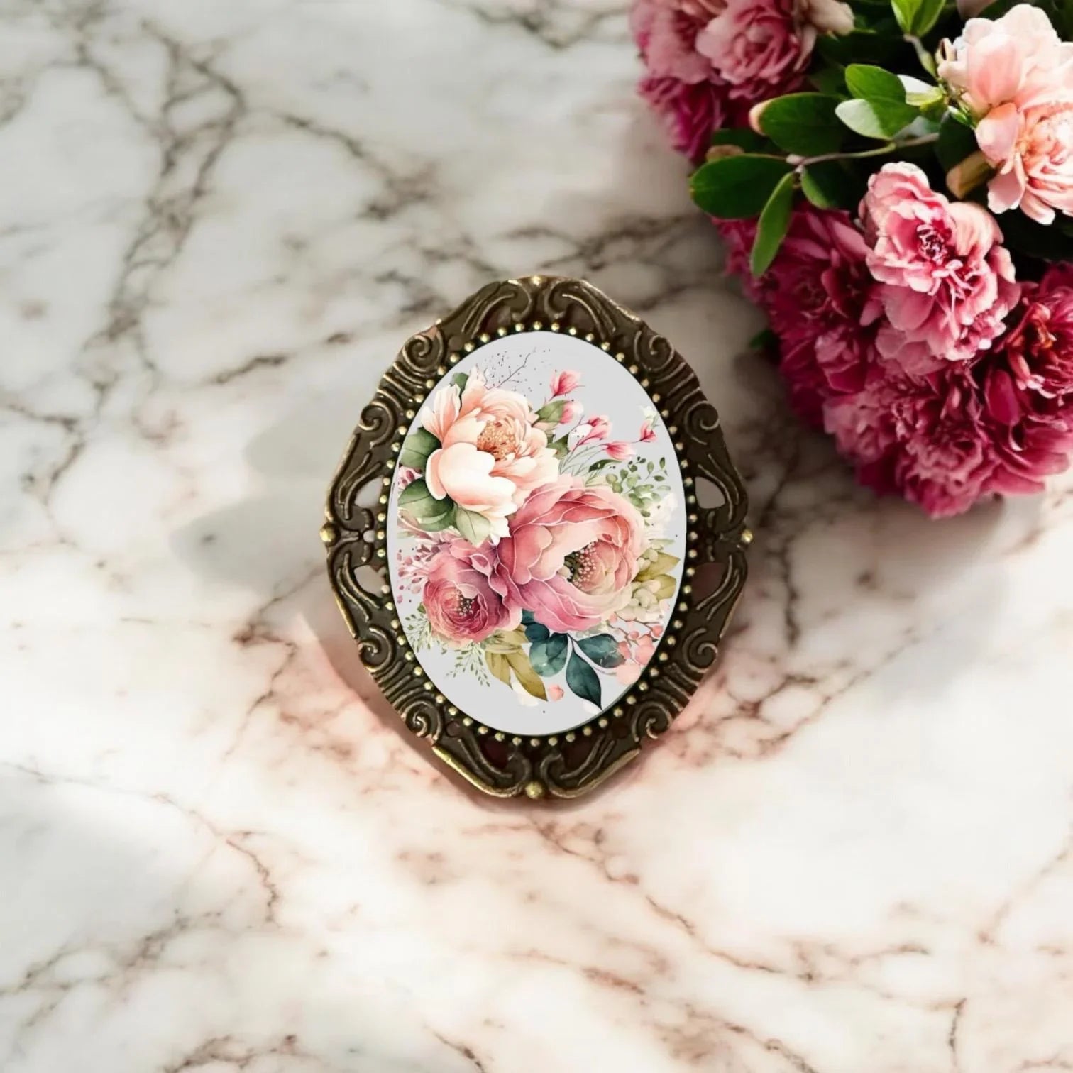 Decorative brooch with floral design on a marble surface with pink flowers.